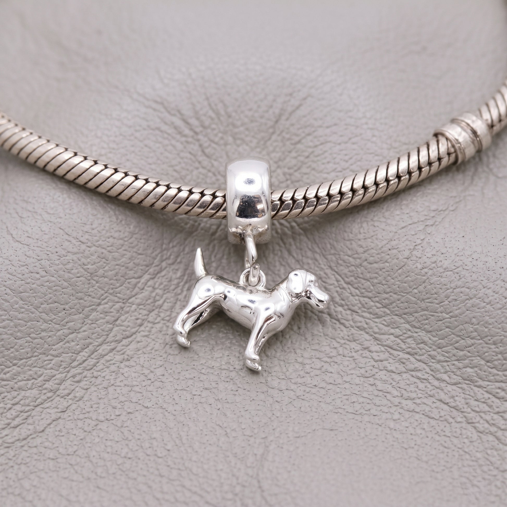 Silver dog charm on a snake chain bracelet against a gray leather background