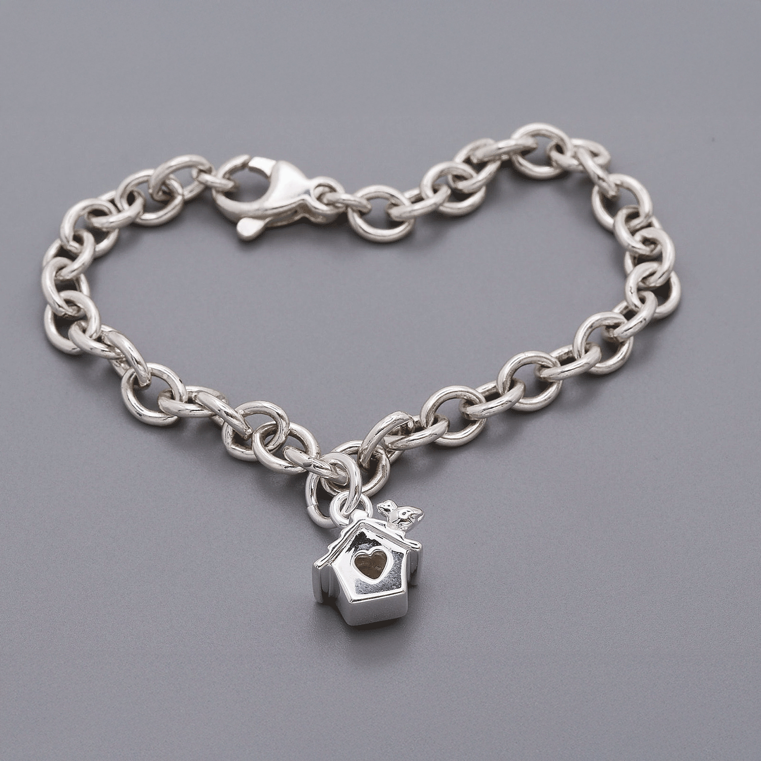 Silver chain bracelet with a heart-shaped birdhouse charm on a gray background
