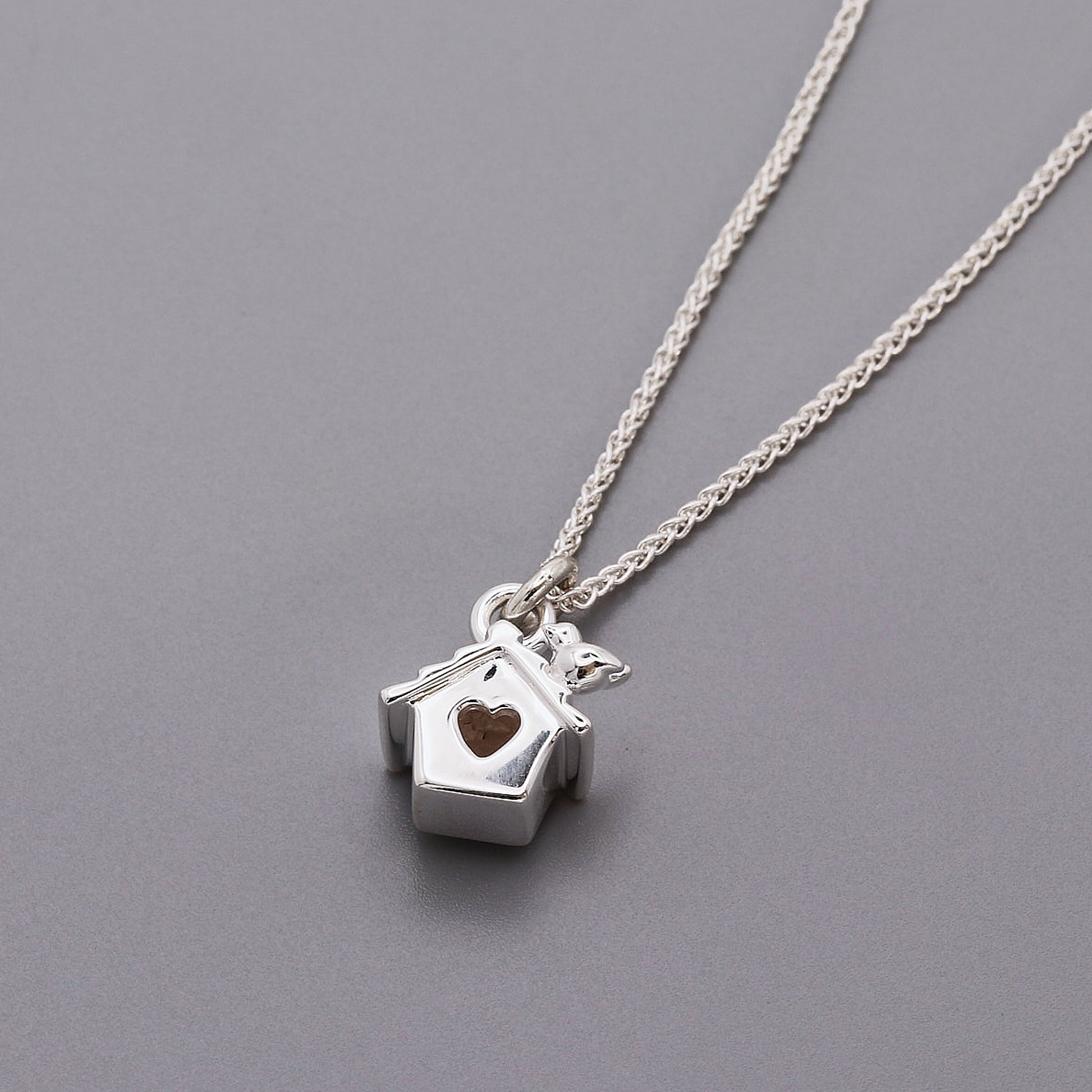 Silver necklace with a birdhouse pendant featuring a heart on a gray background