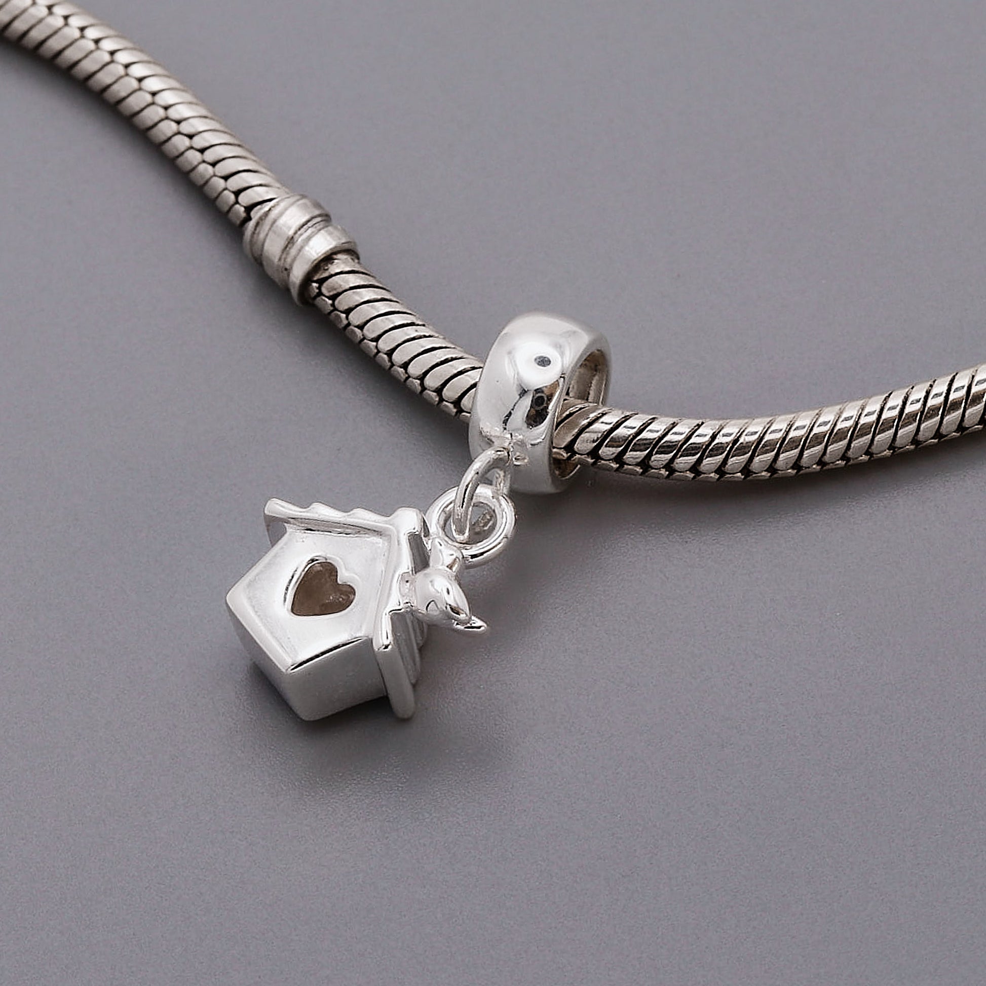 Silver bracelet with a birdhouse charm on a gray background
