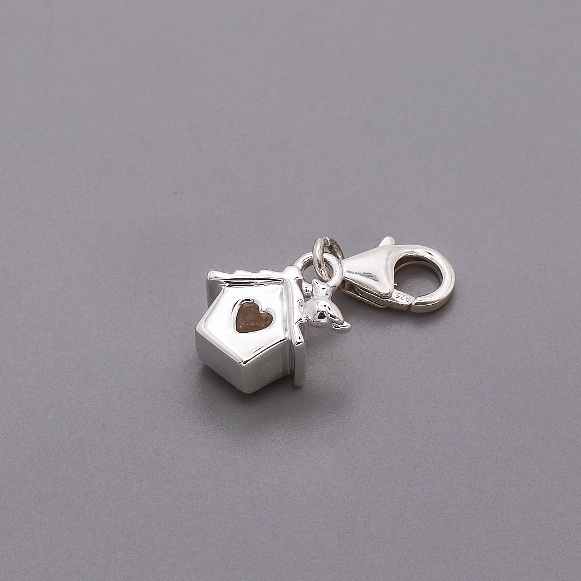 Silver charm with a heart and bird box design on a gray background