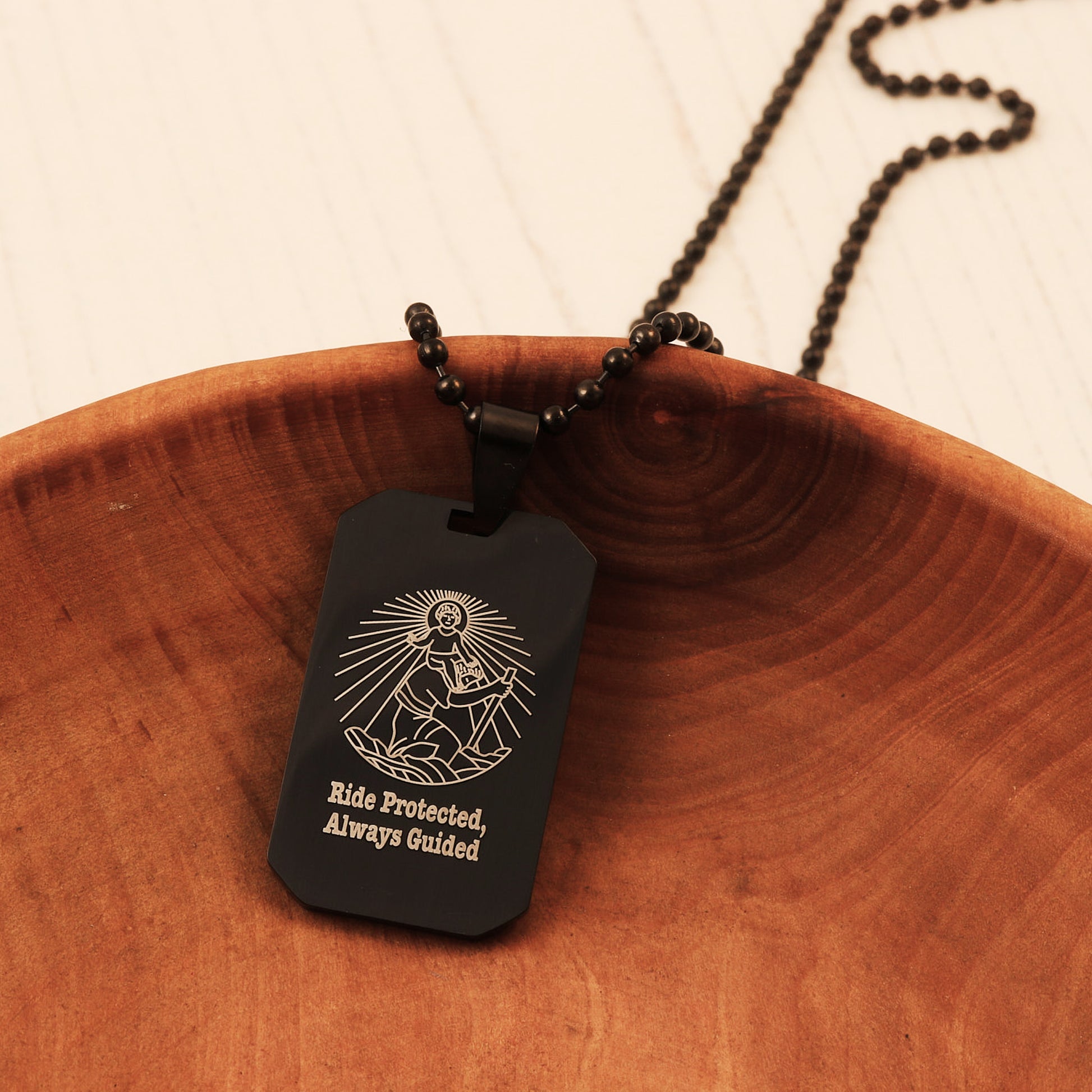 Black dog tag necklace with engraved design and text on a wooden surface