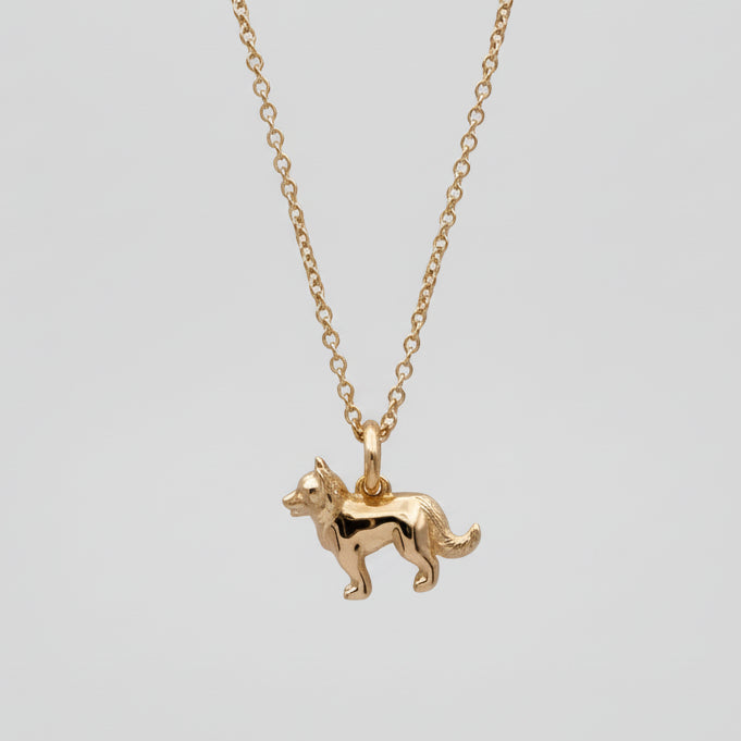 Gold dog-shaped pendant on a chain against a light purple background