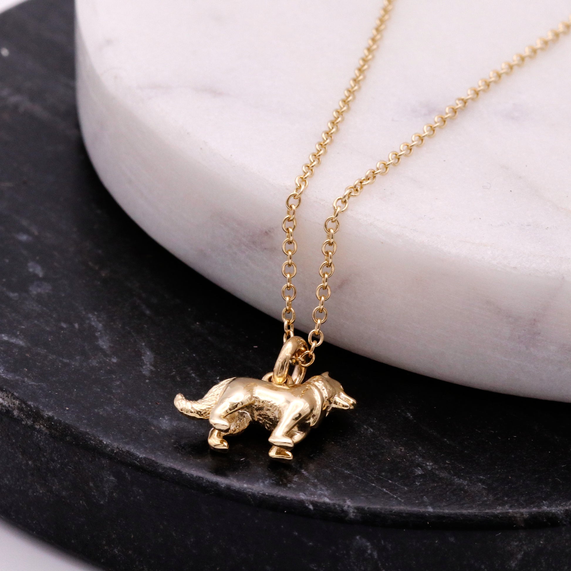 Gold border collie pendant necklace on a marble and slate background