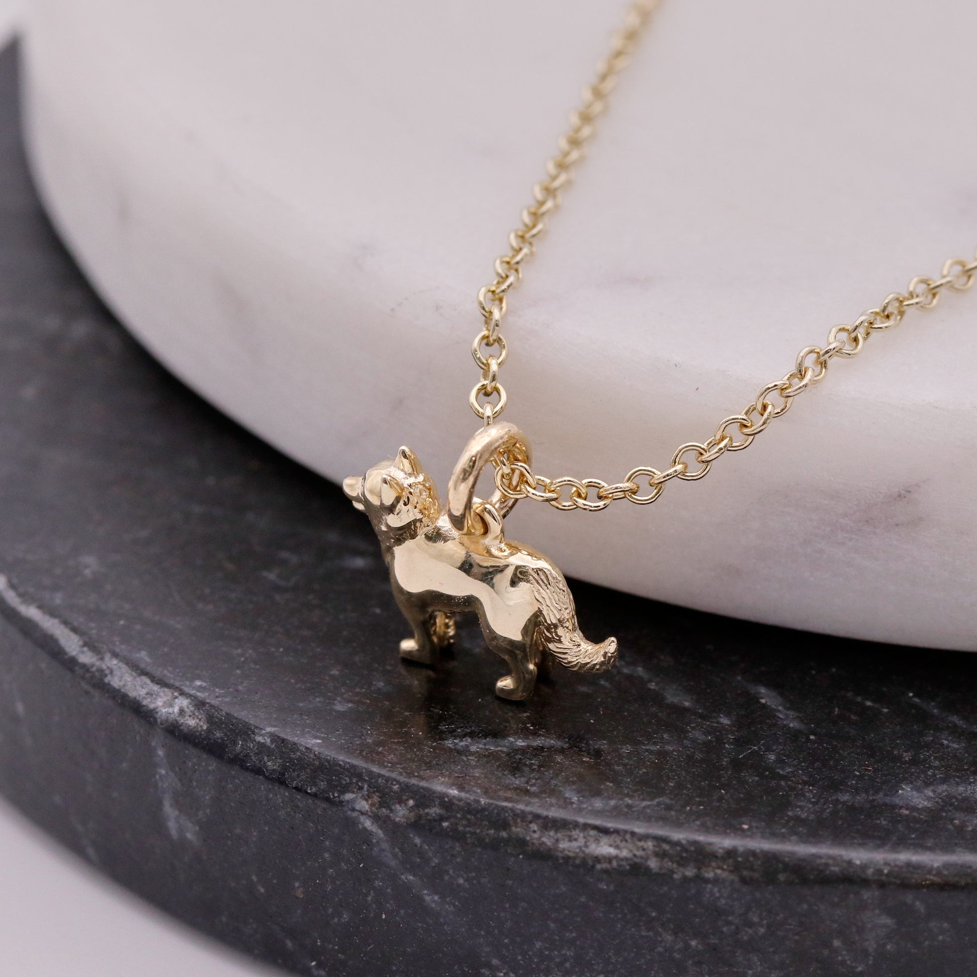Gold dog-shaped pendant necklace on a marble and stone surface