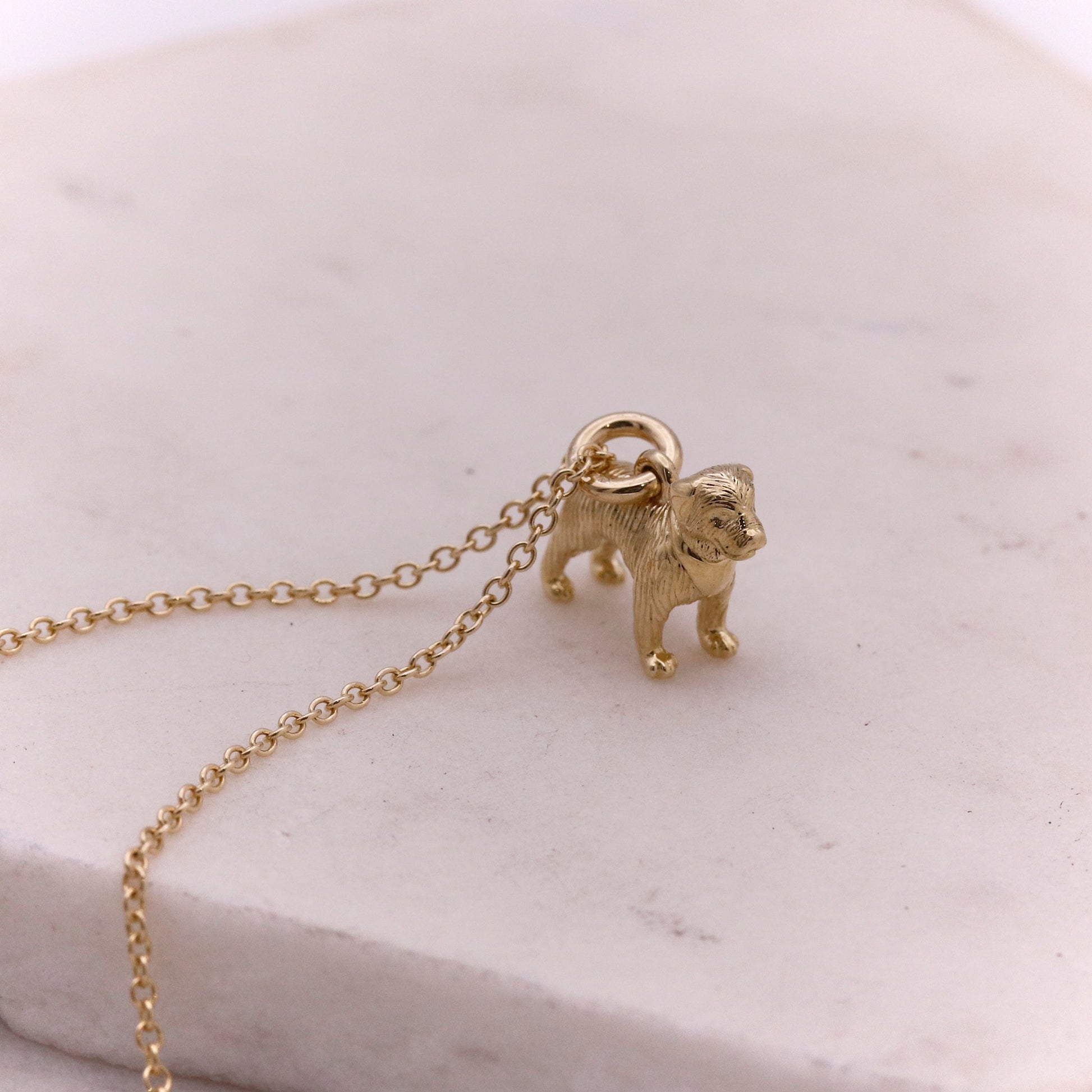 Gold dog-shaped pendant on a chain against a light marble background