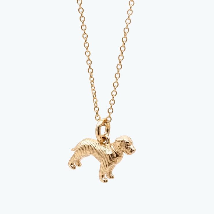 Gold dog-shaped pendant on a chain against a light pink background
