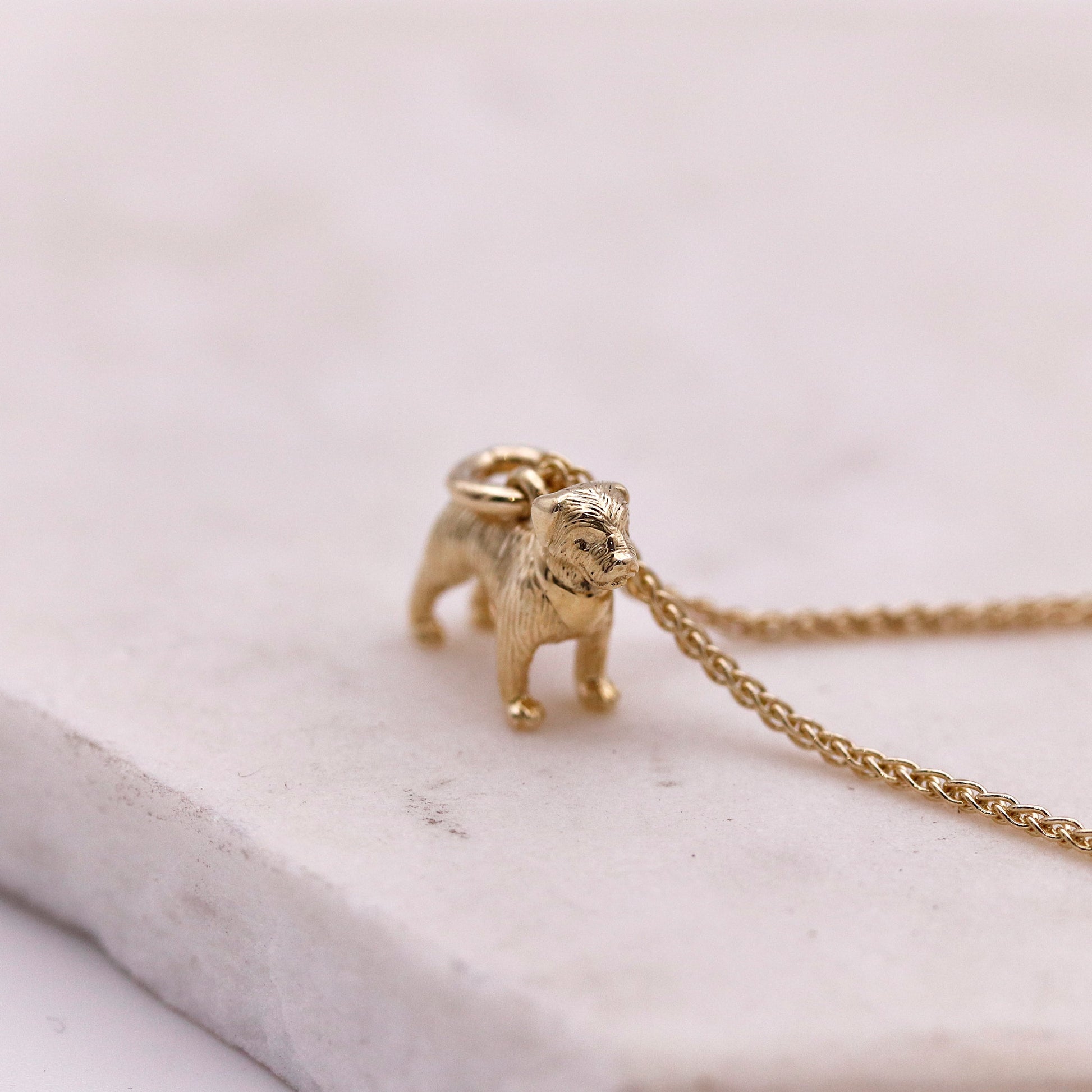 Gold border terrier pendant on a chain against a light background