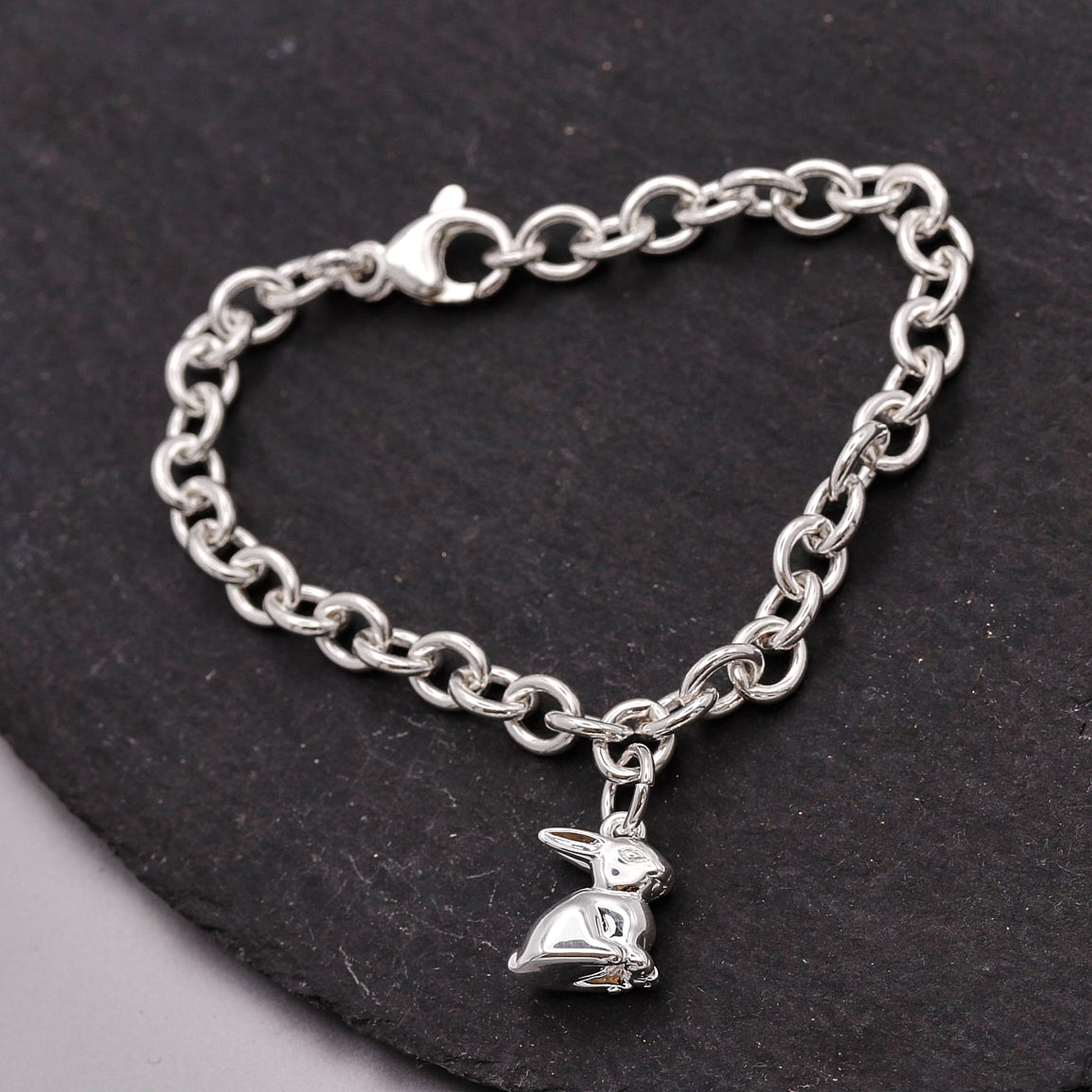 Silver chain bracelet with a bunny charm on a dark stone surface