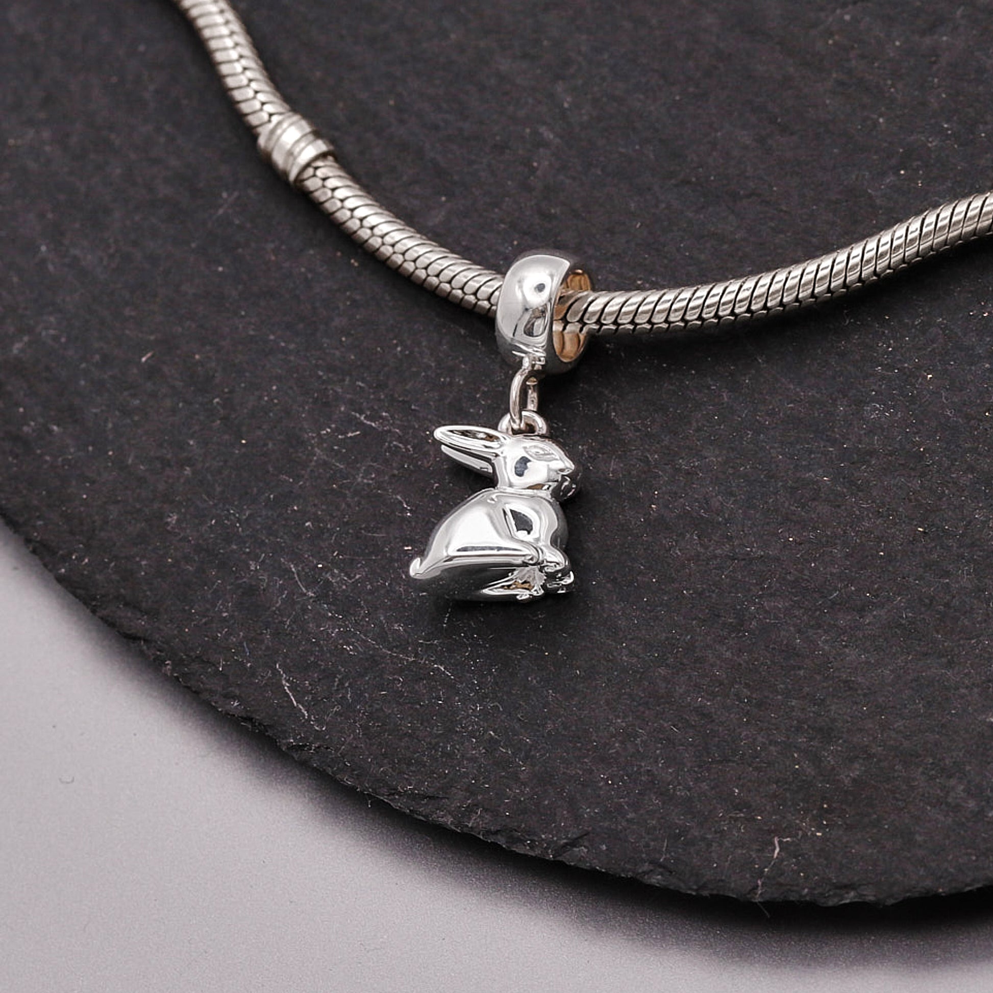 Silver charm shaped like a rabbit on a snake chain against a dark background