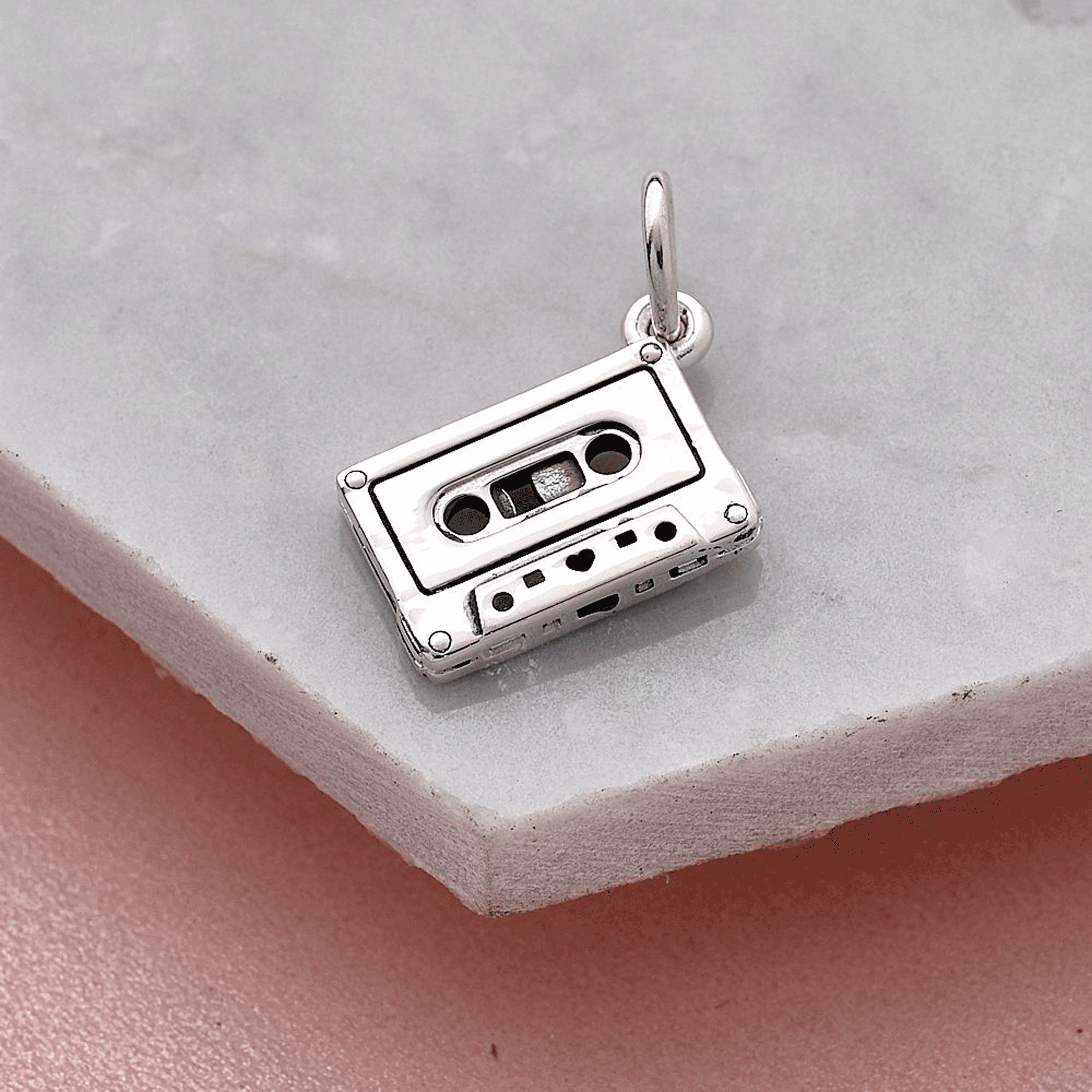 Silver cassette tape charm on a light gray surface without engraving