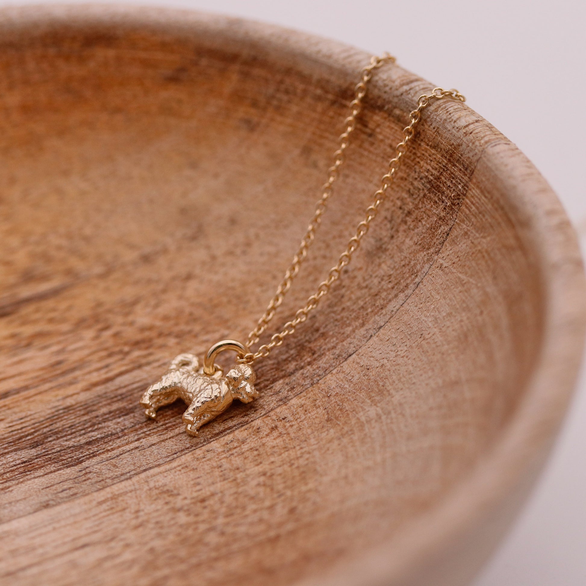 Gold necklace with a cavapoo pendant on a wooden surface