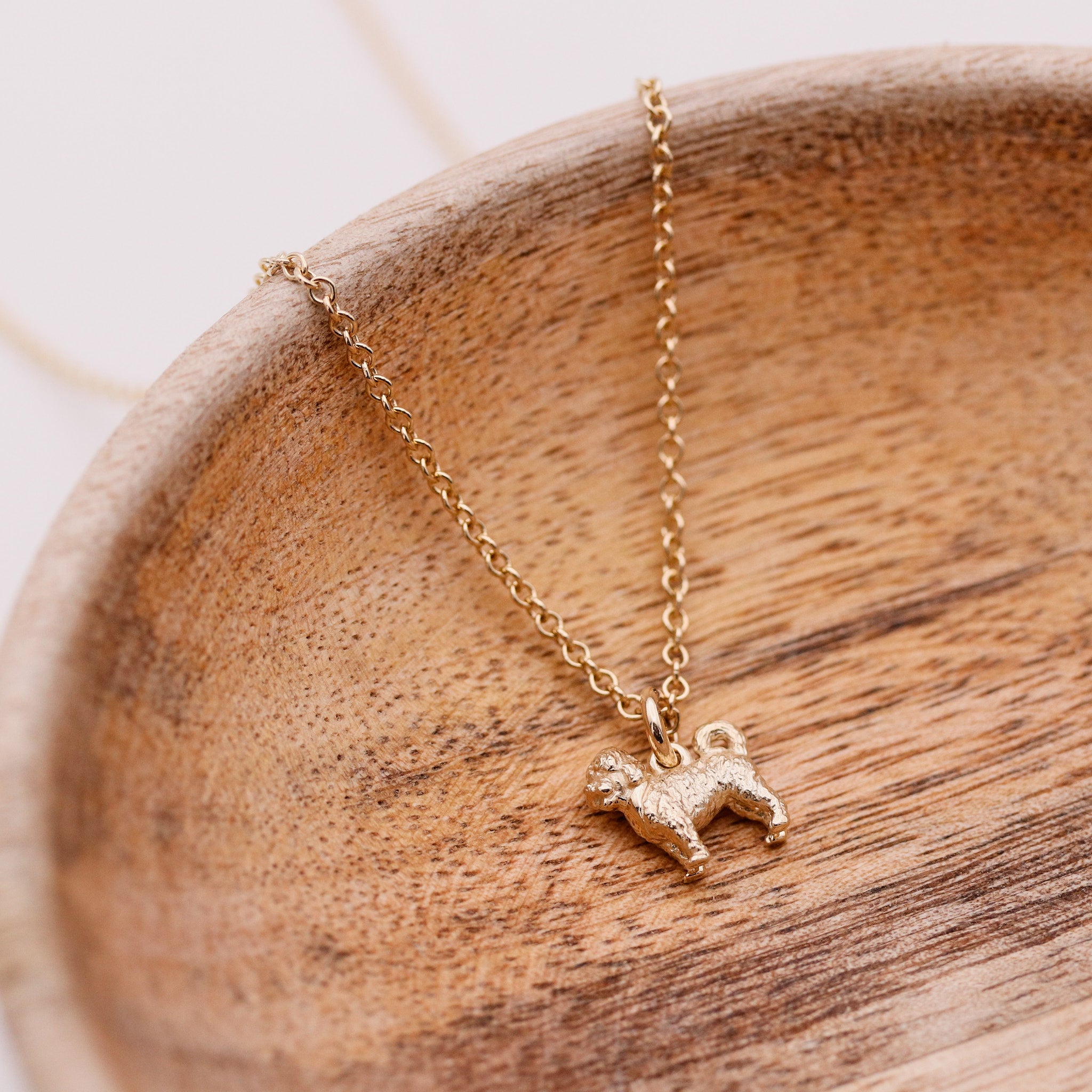 Gold necklace with a cavapoo dog pendant on a wooden surface
