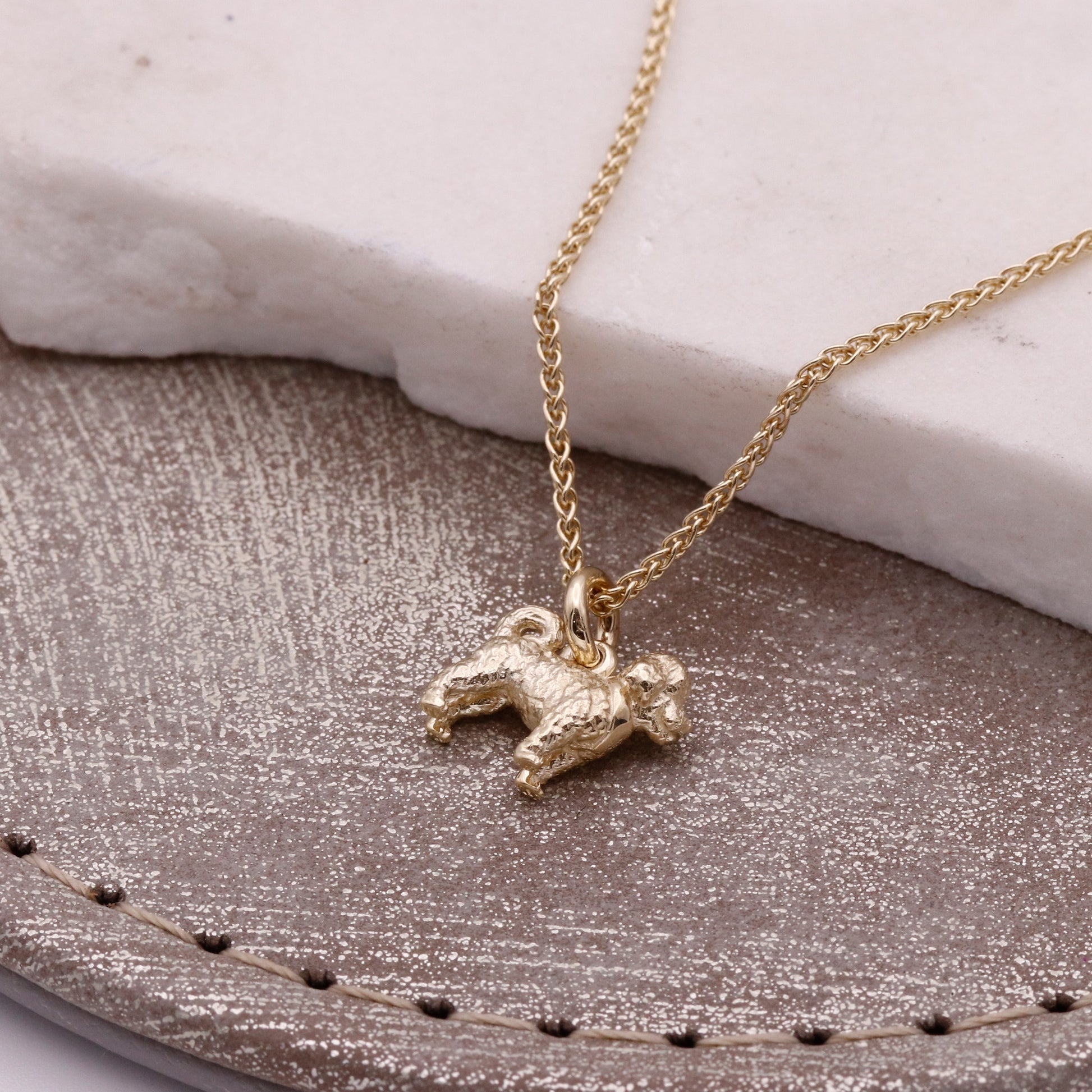 Gold necklace with a cavapoo pendant on a textured surface