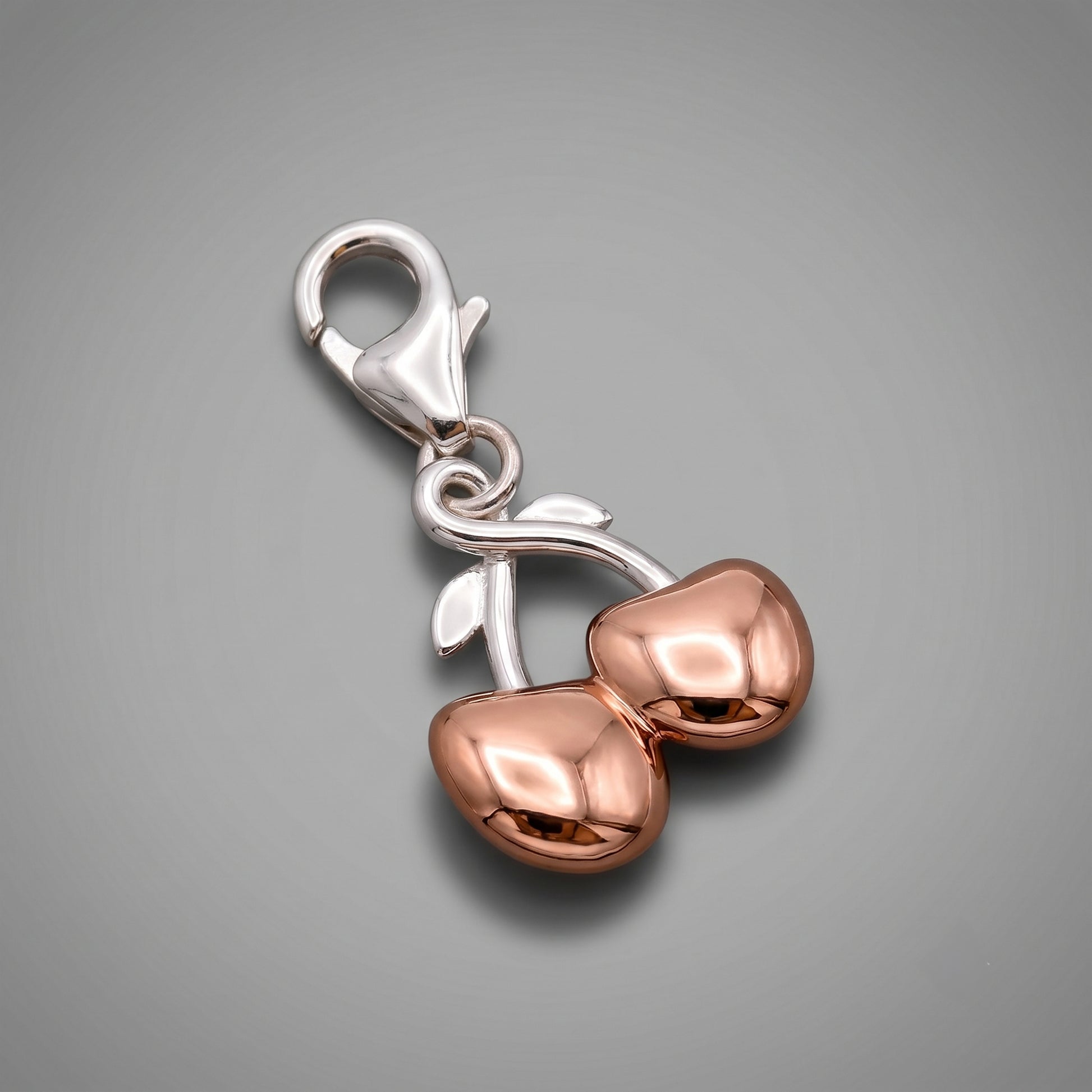 Rose gold and silver cherry-shaped charm on a gray background