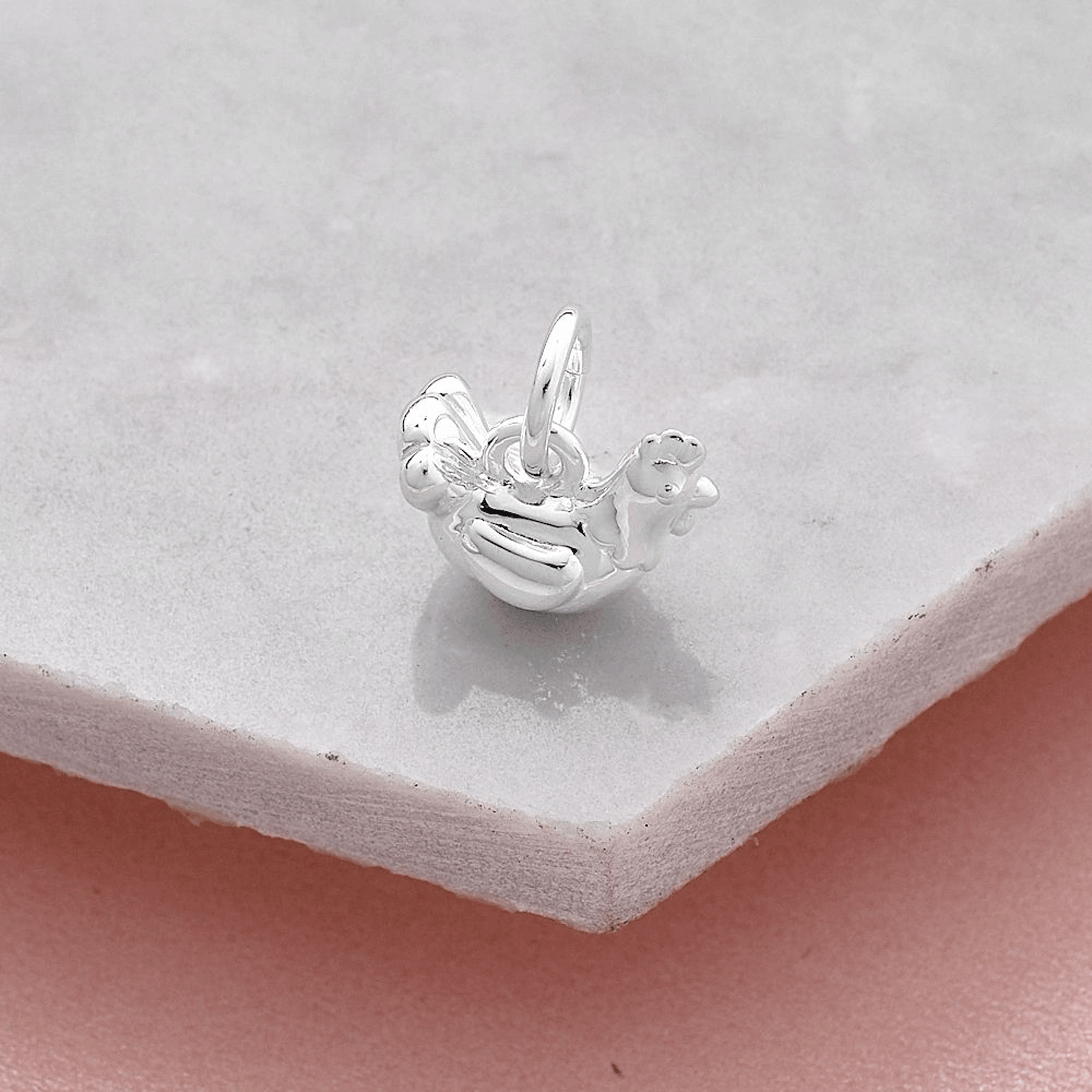 Silver rooster chicken hen charm on a light gray surface