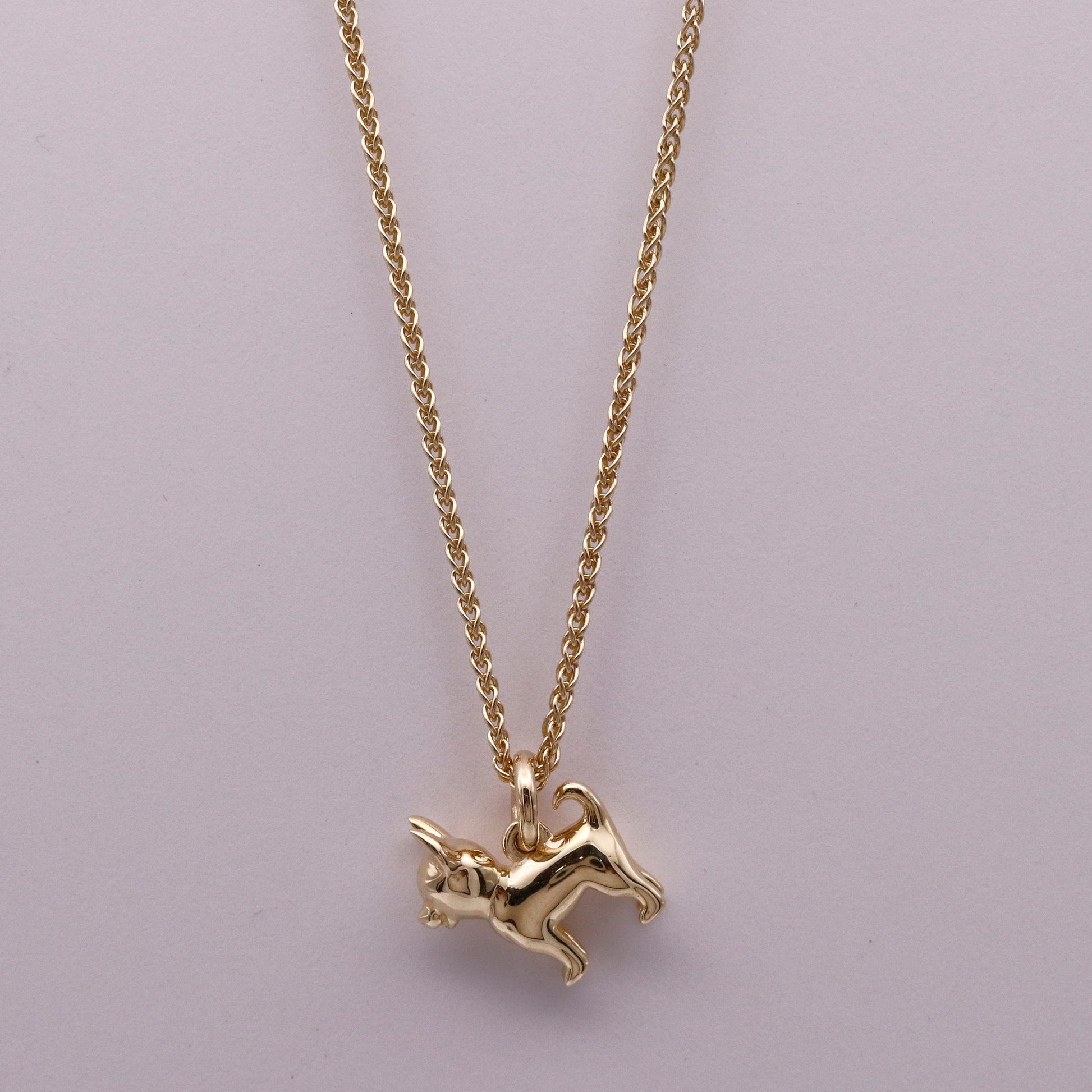 Gold dog-shaped pendant on a chain against a light purple background