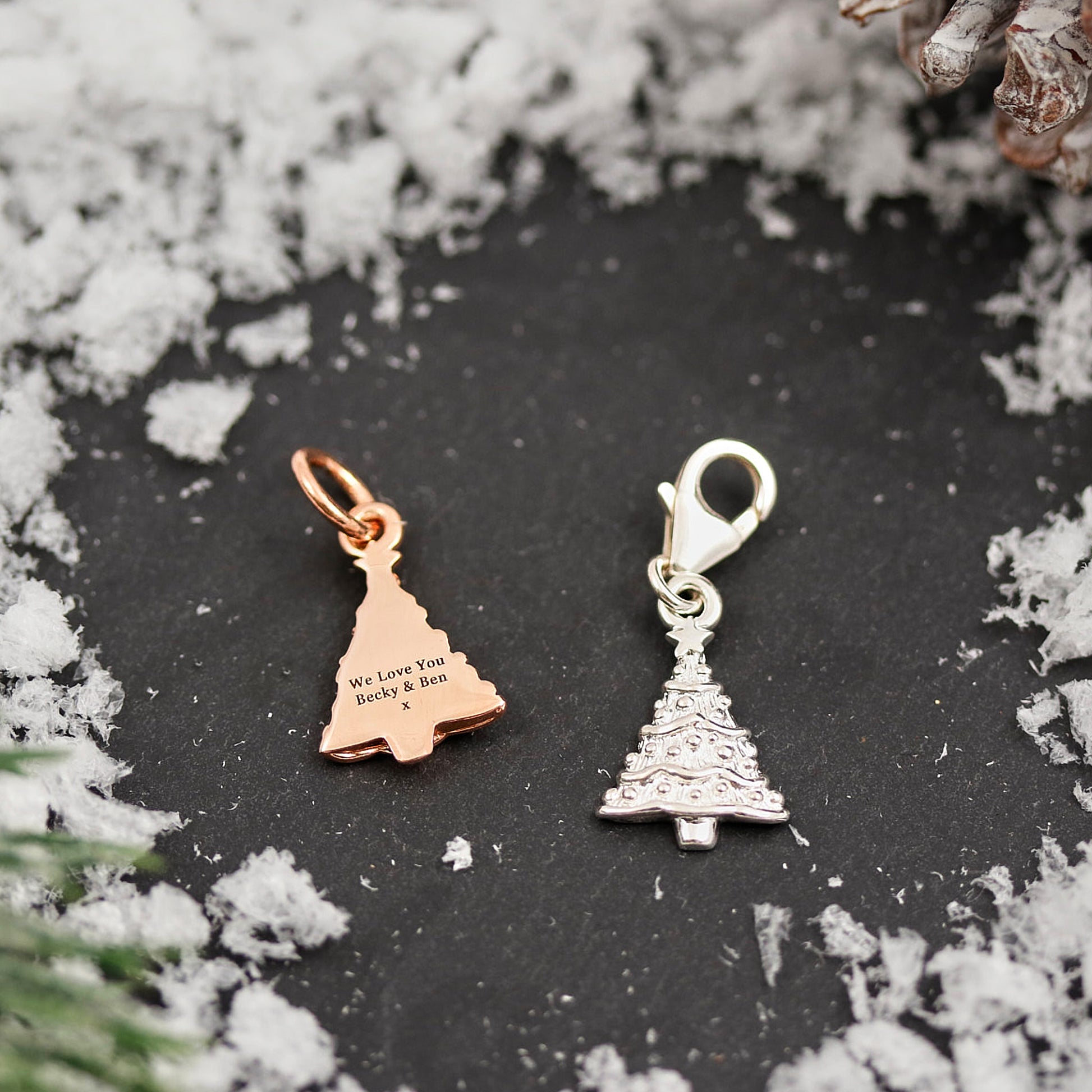 Two Christmas tree-shaped charms on a dark surface with snowflake decorations.