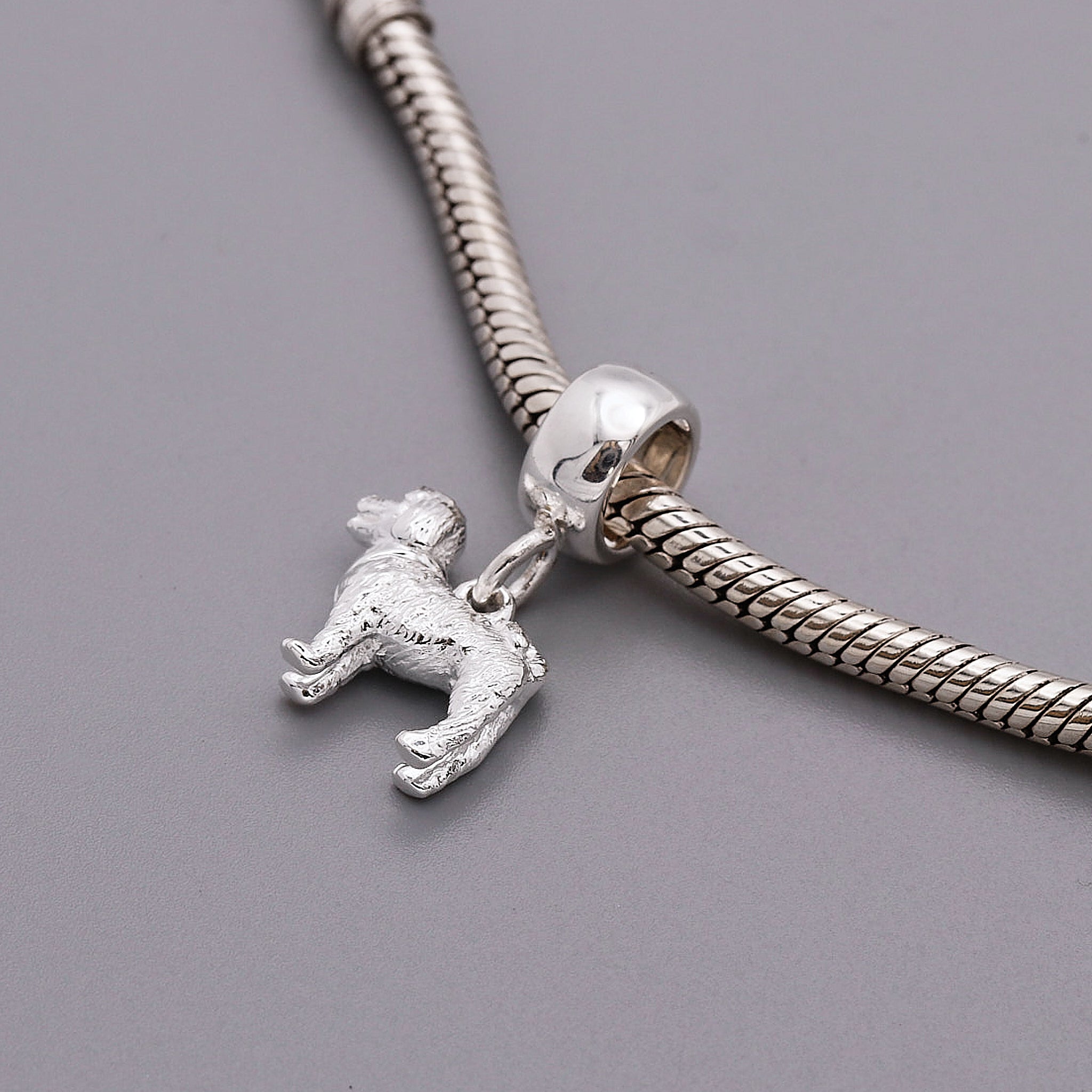 Silver charm with a dog design on a snake chain against a gray background