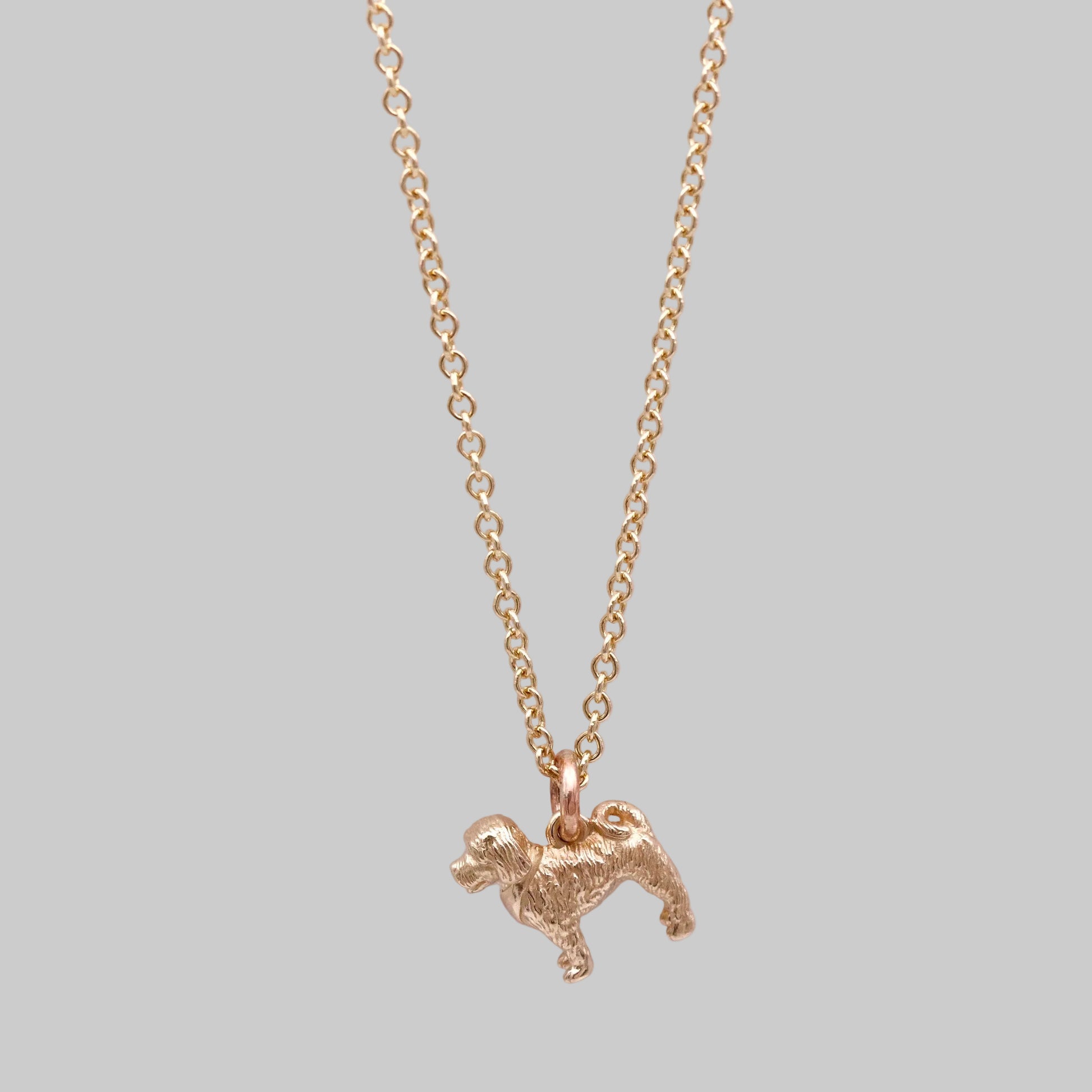 Gold necklace with a small cockerpoo dog pendant on a light pink background
