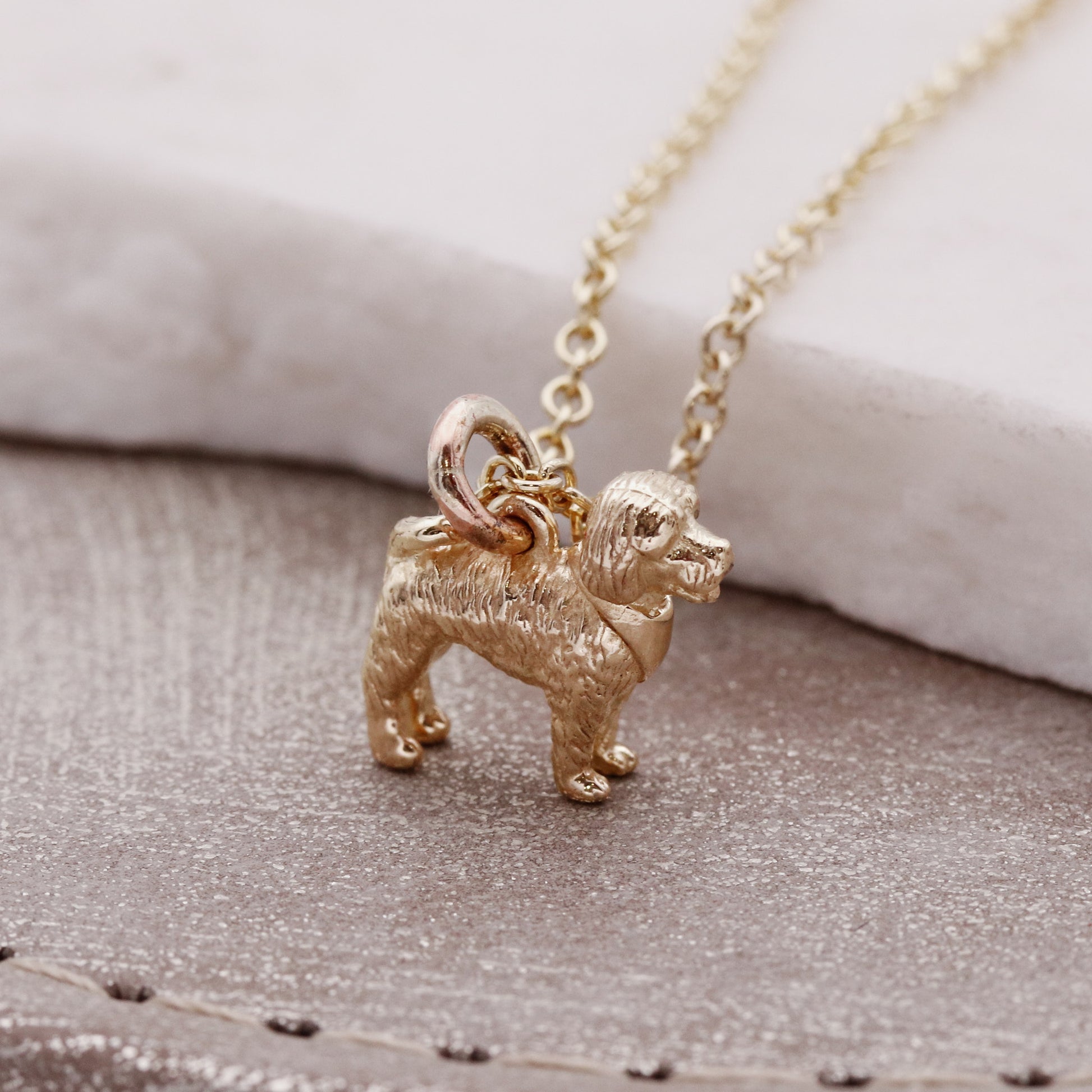 Cockapoo gold dog-shaped pendant on a chain against a neutral background