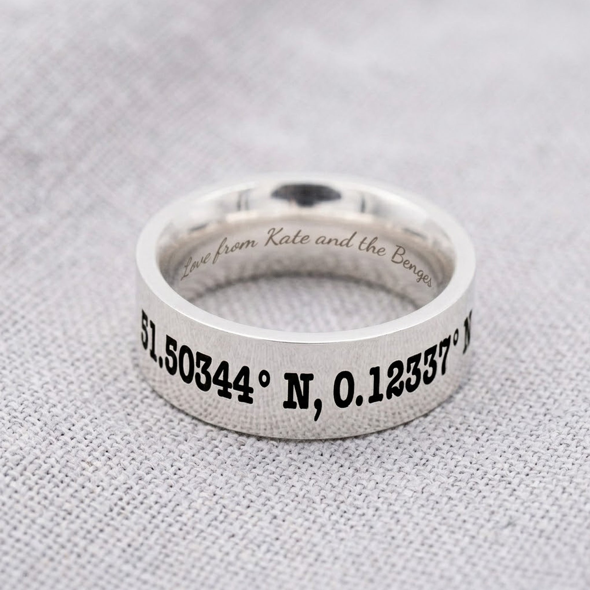 Silver ring with engraved coordinates on a gray fabric background