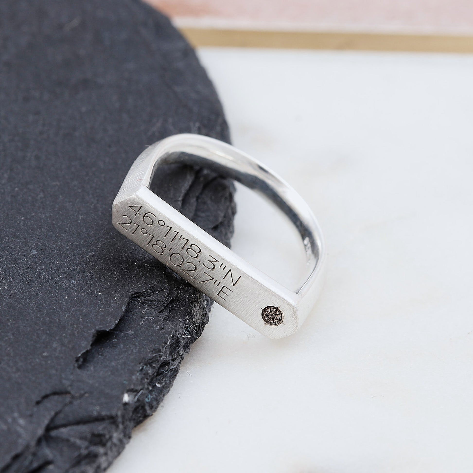 Silver matte finish bar signet ring with engraved coordinates on a dark stone surface