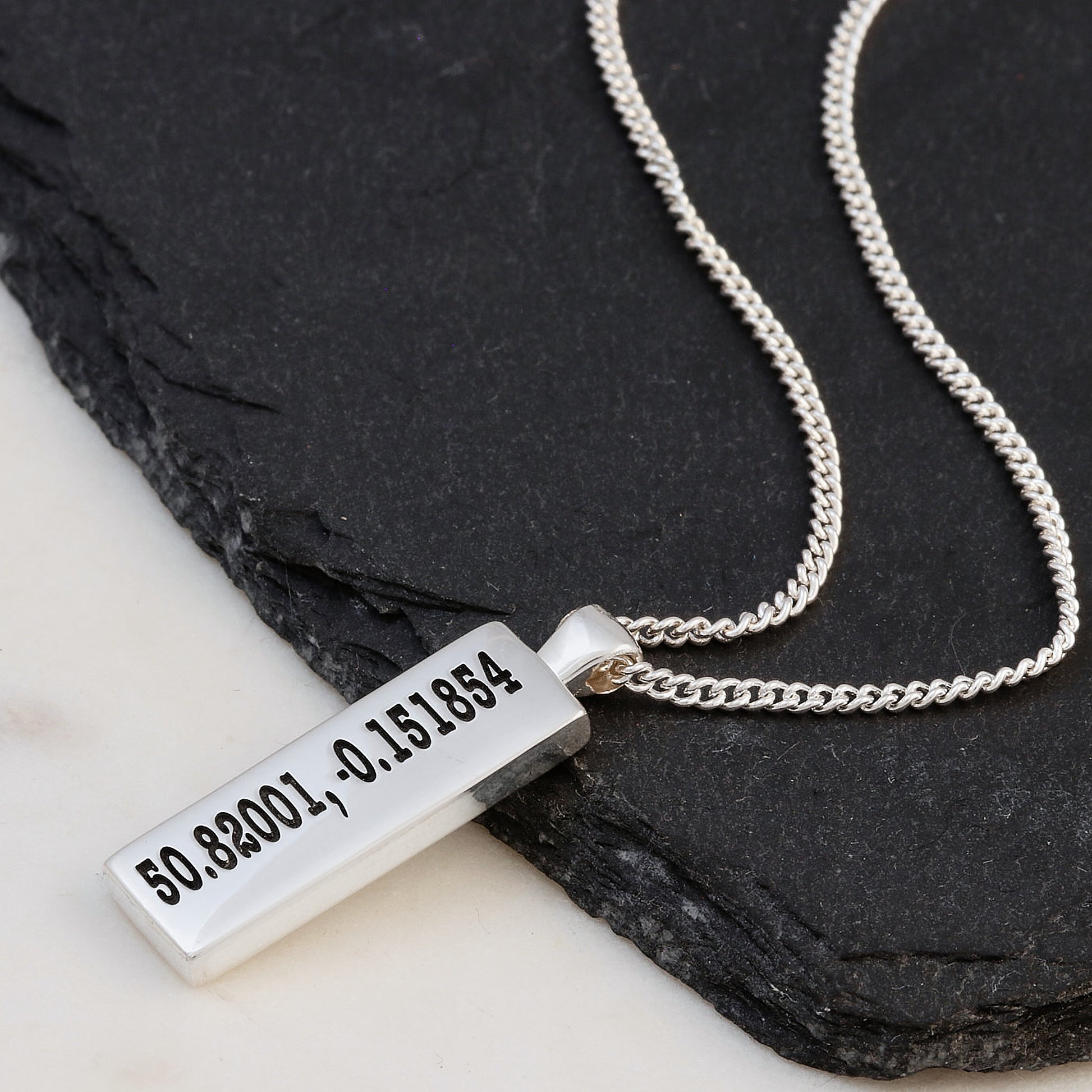 Silver latitude longitude personalised necklace with a rectangular pendant on a dark stone surface