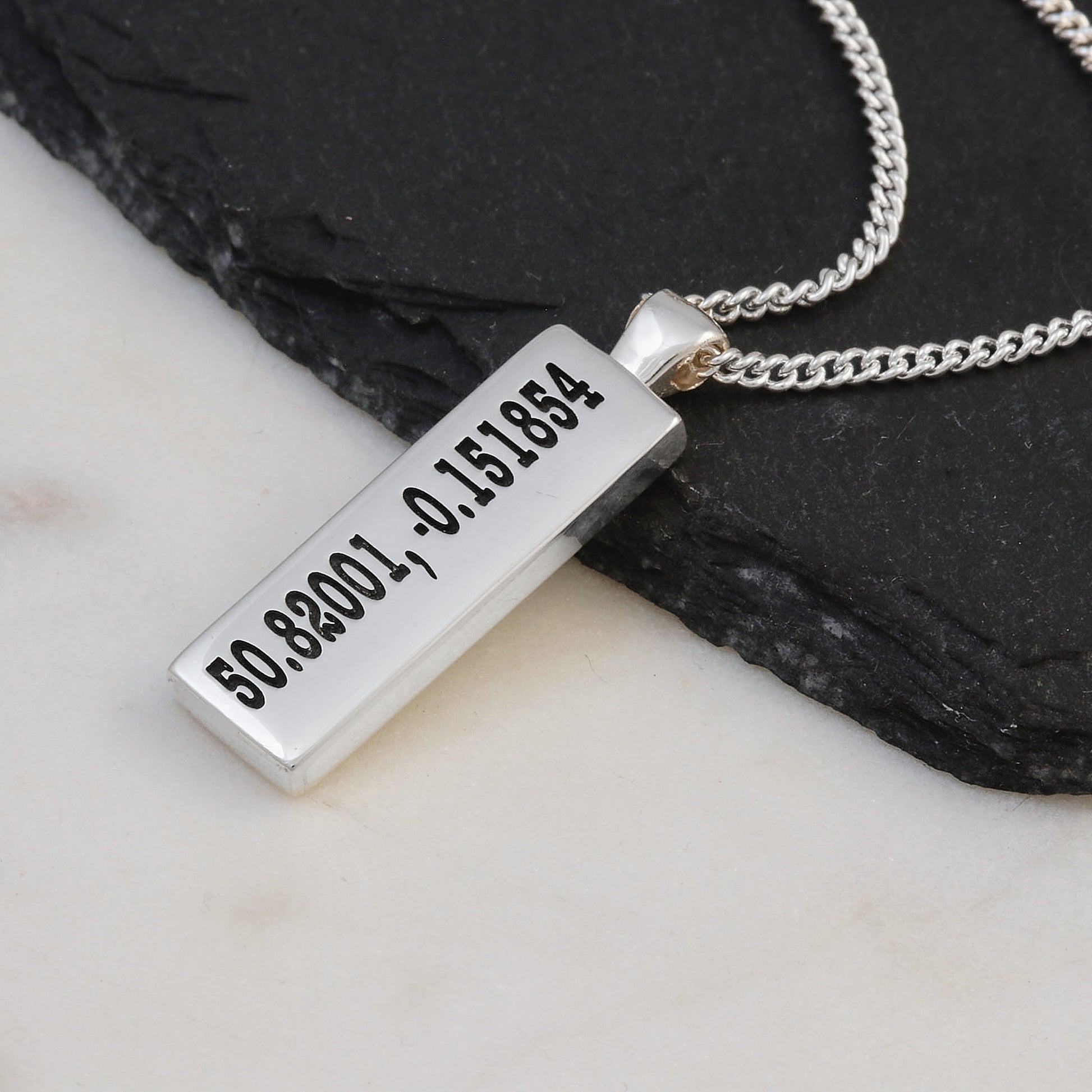 Silver pendant with engraved coordinates on a dark stone surface
