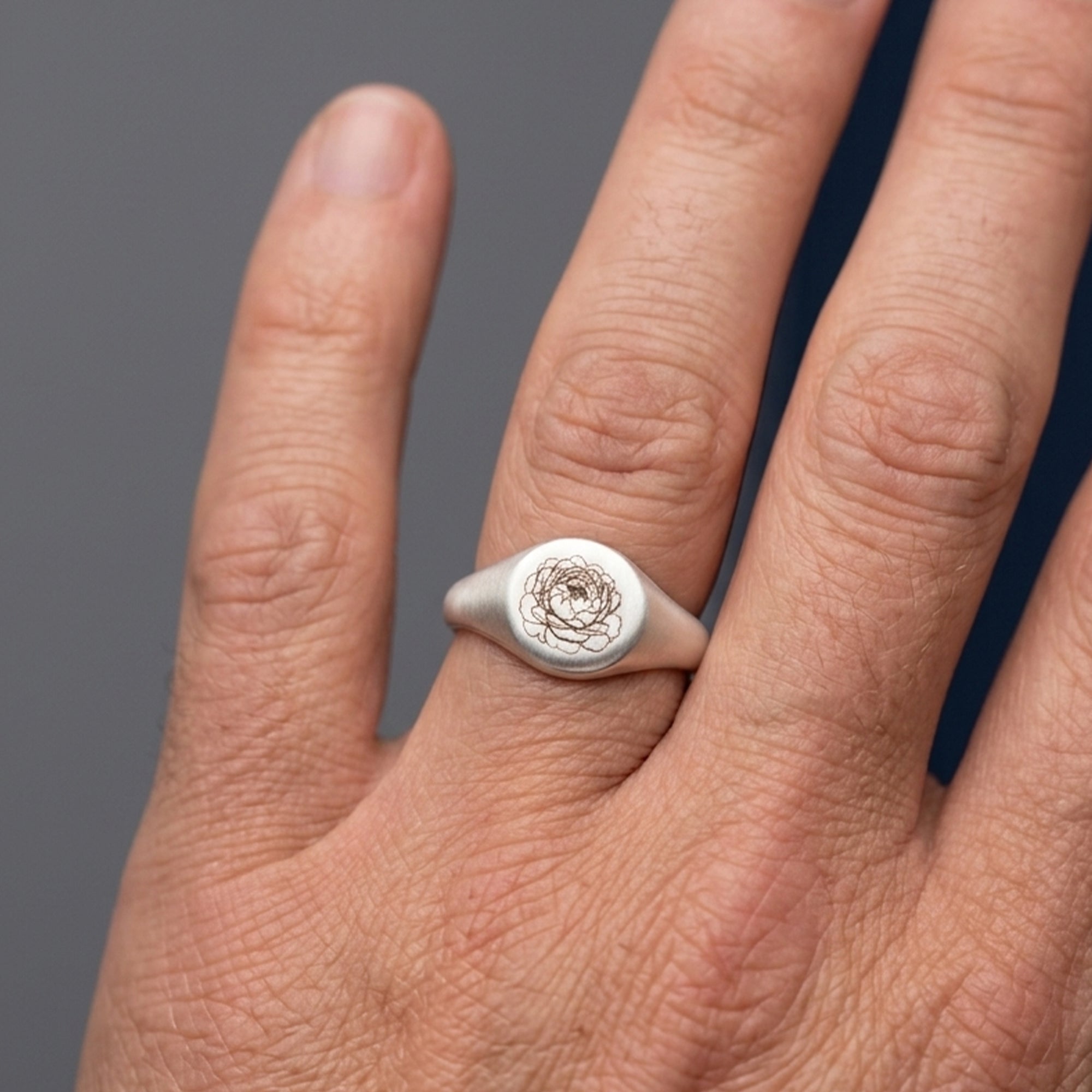 custom signet ring engraved with flower design on a finger with grey and navy background