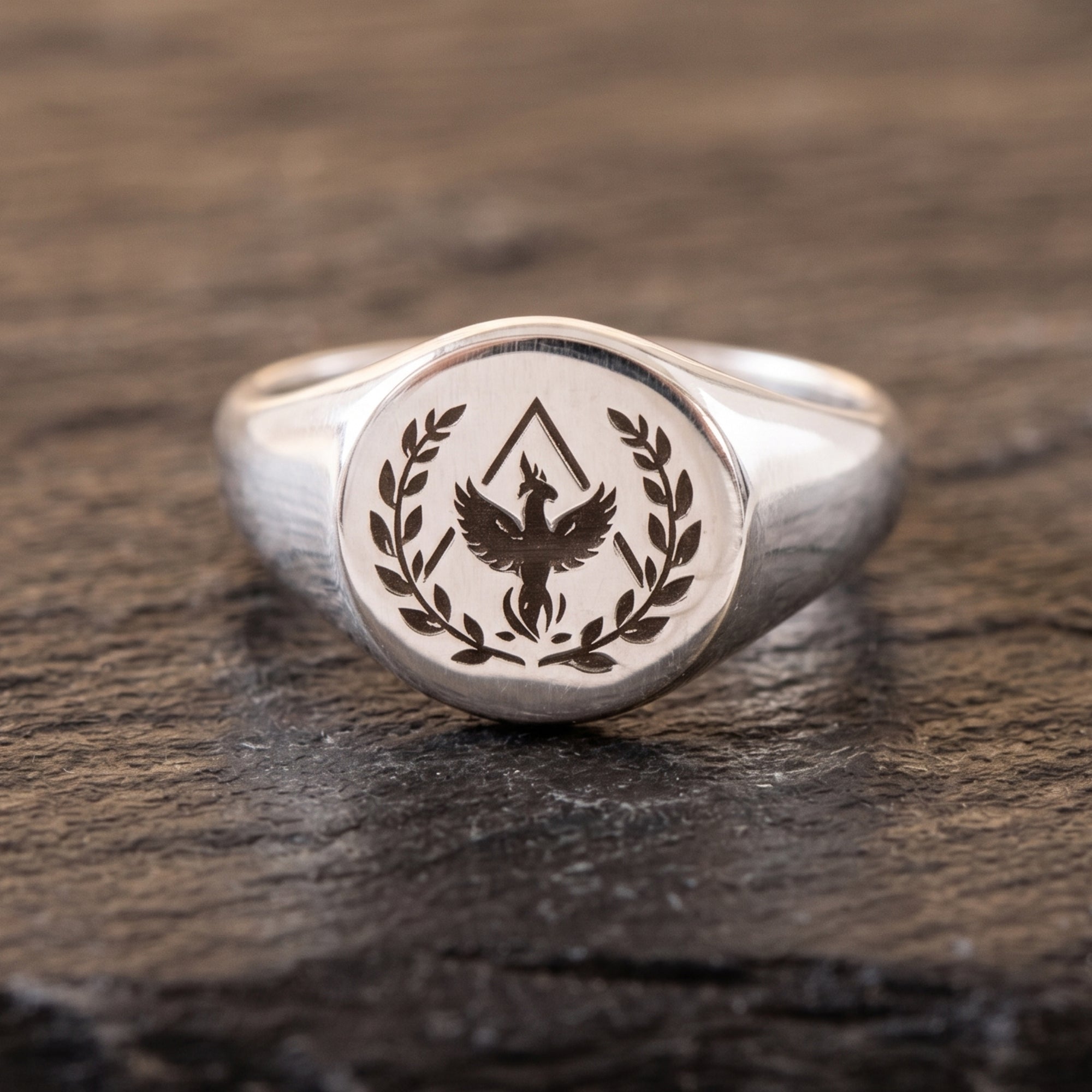 A silver signet ring featuring an engraved eagle and laurel wreath emblem, resting on a dark textured wooden surface.