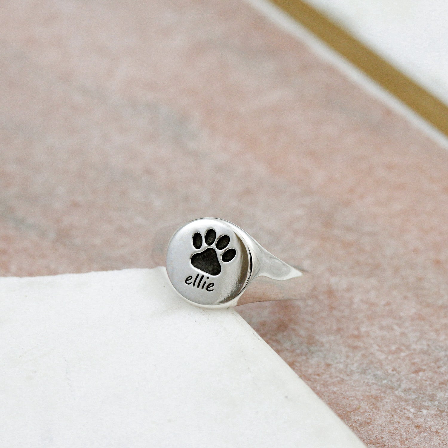 Silver ring with paw print and 'ellie' engraving on a soft surface