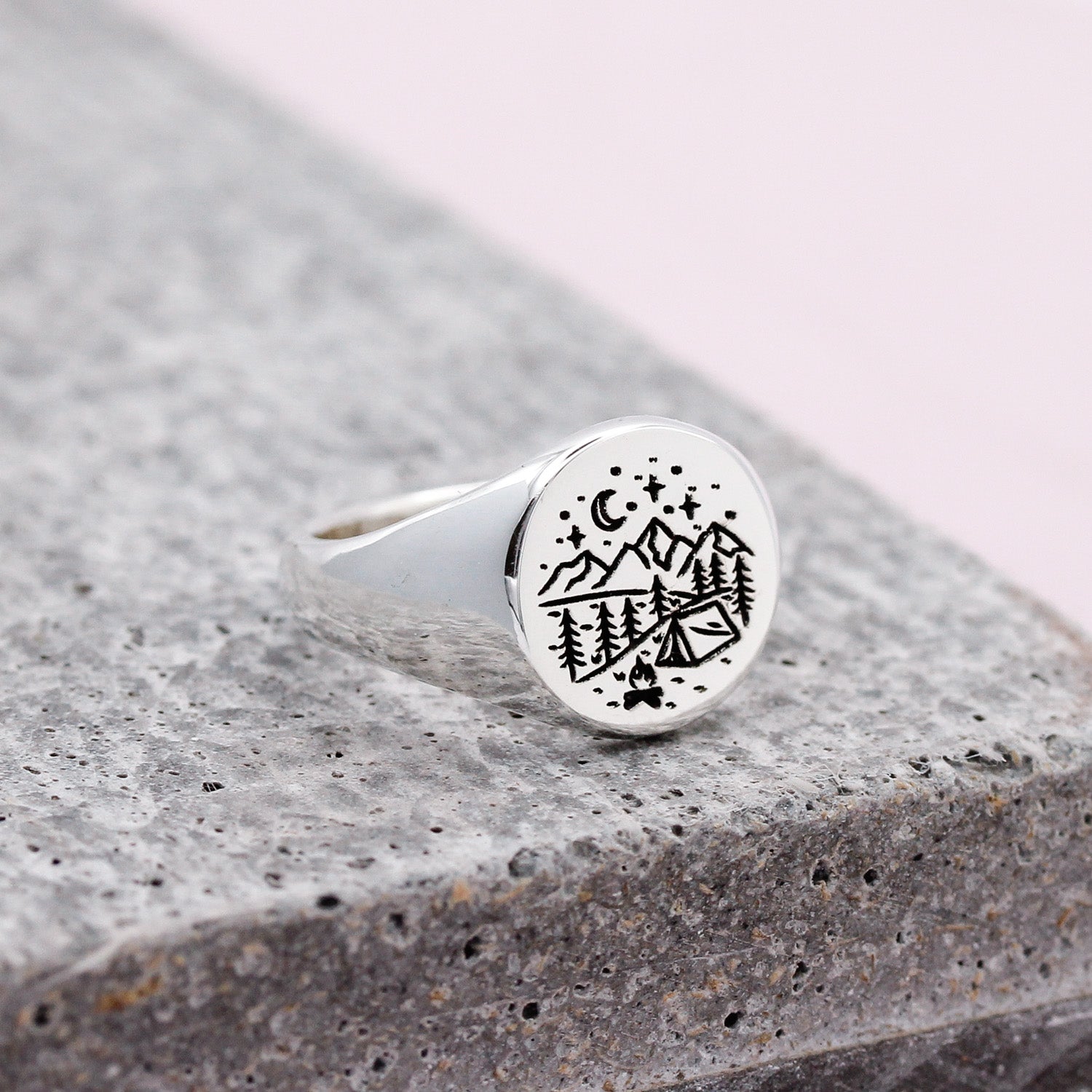 Silver ring with black engraved outdoors camping design on a stone surface
