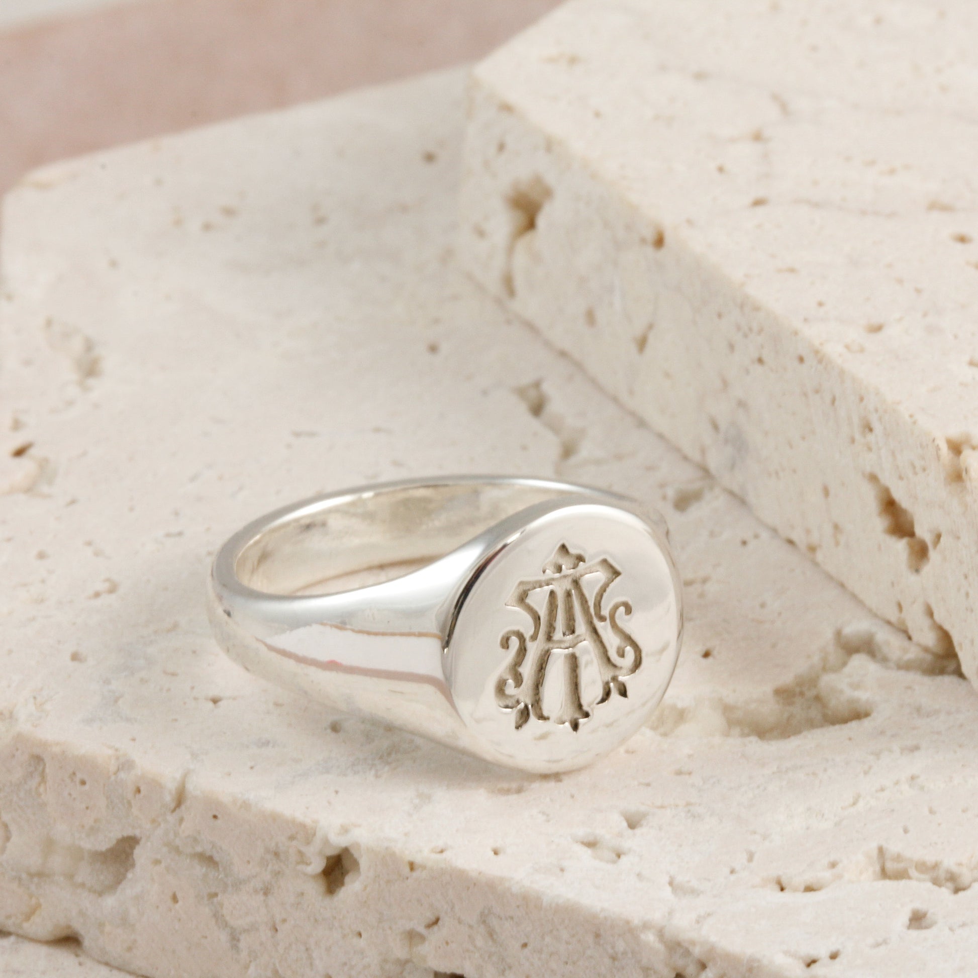 Silver ring with a monogram on a textured beige surface