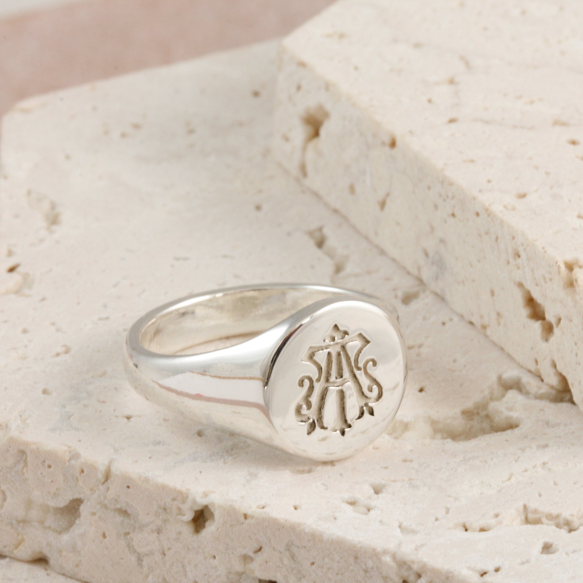 Silver ring with a monogram on a textured beige surface