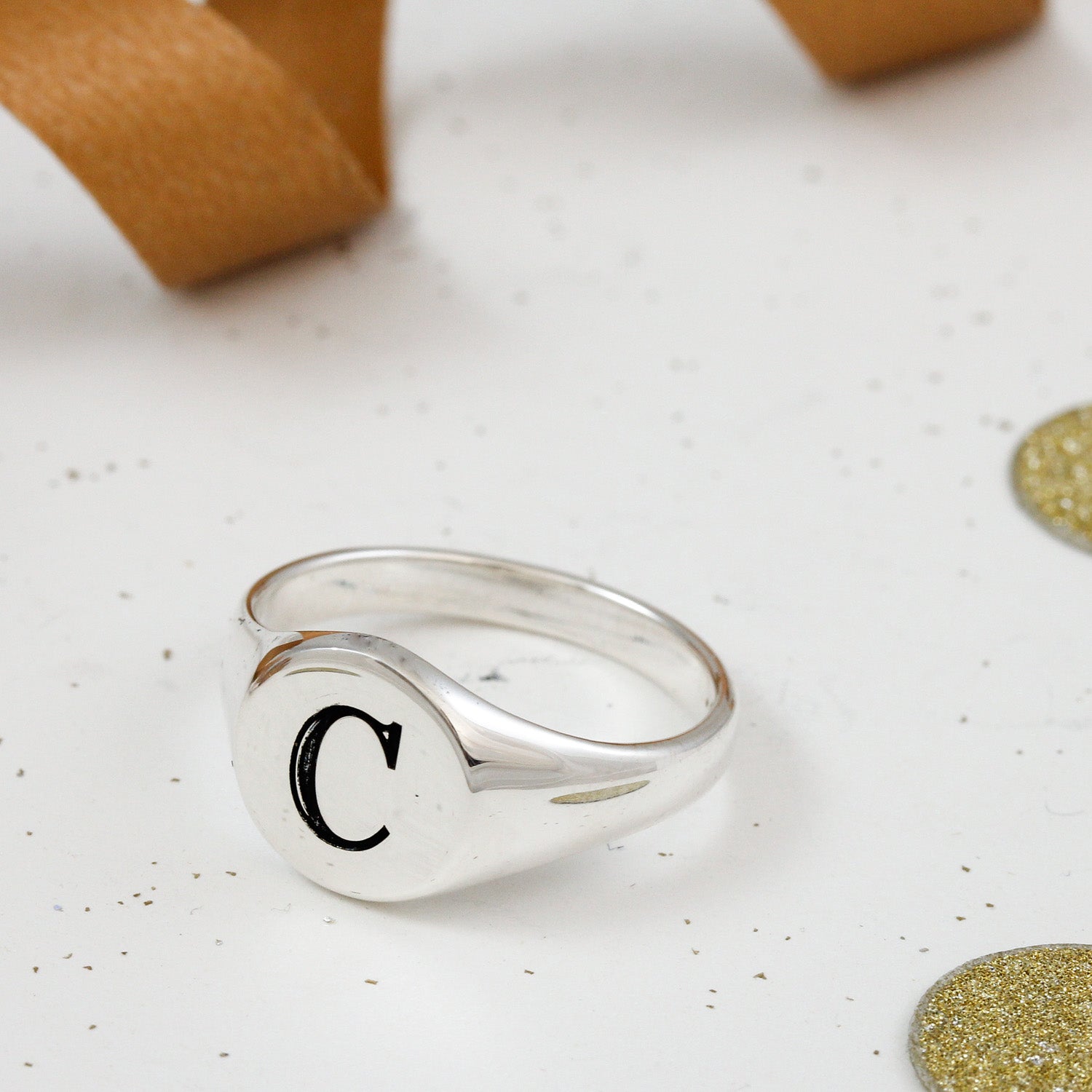 Silver ring with letter 'C' on a textured white surface