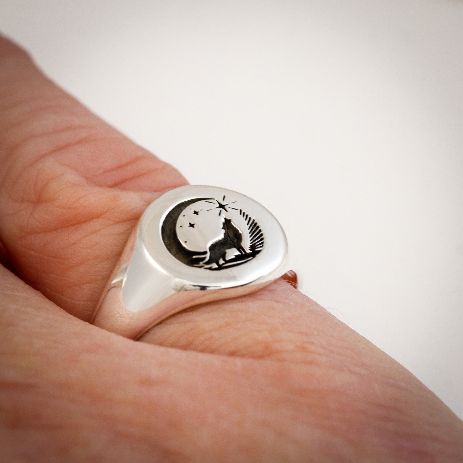 Silver ring with wolf design on a finger against a white background