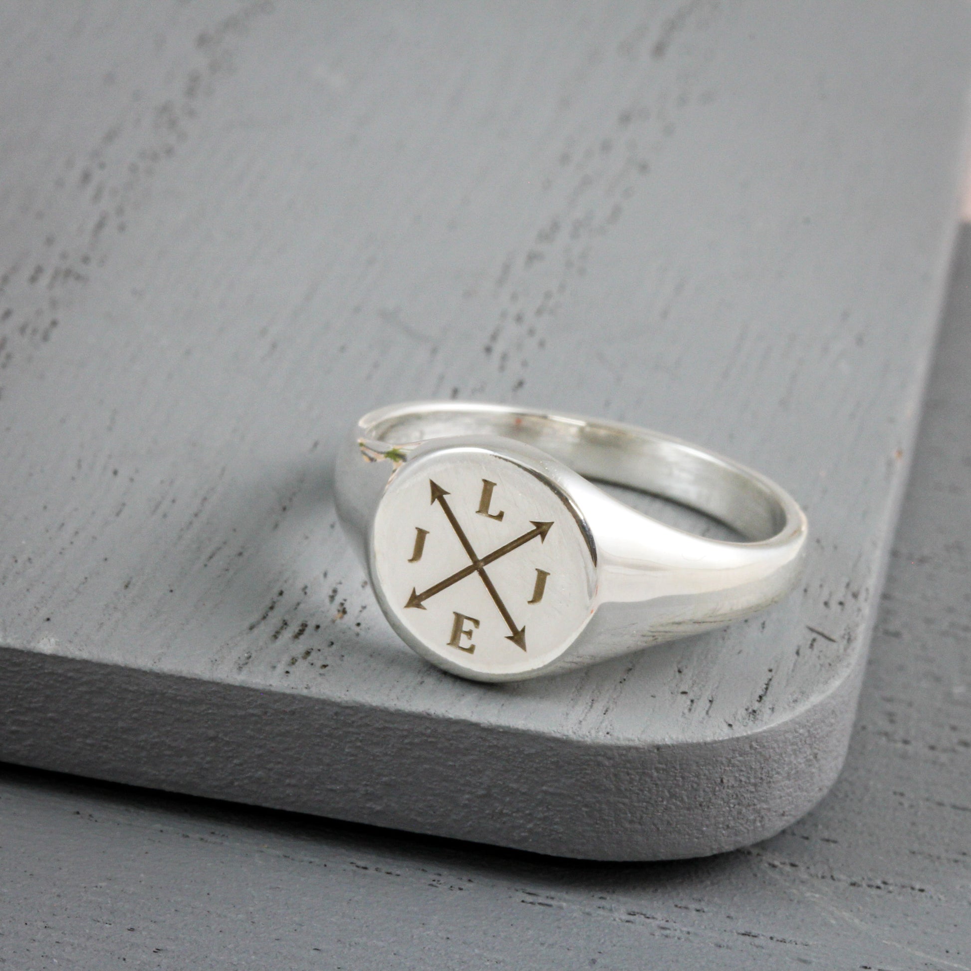 polished silver signet ring with engraved initials on grey wood background
