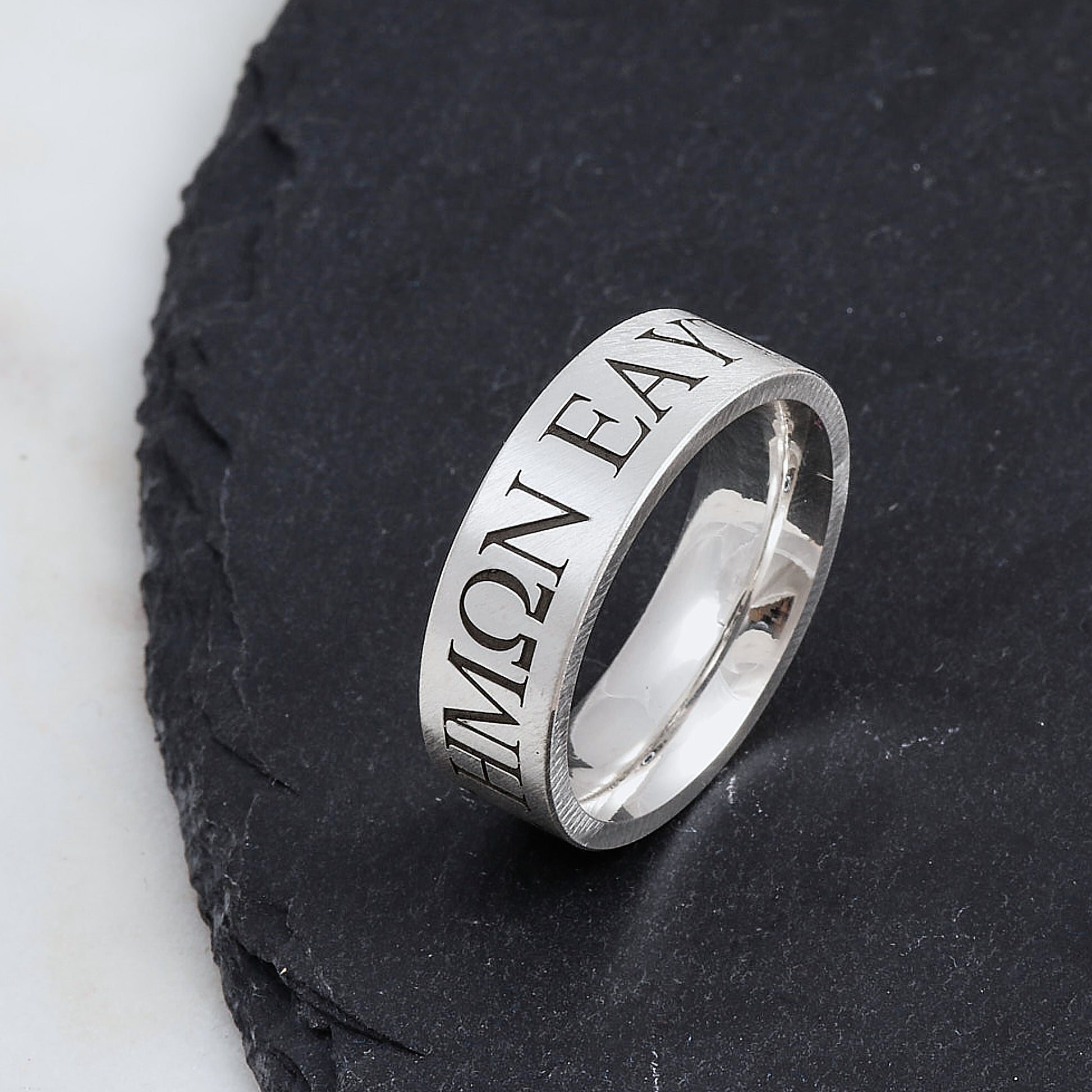 Silver matte finish ring with engraved greek text in serif font on a dark stone surface