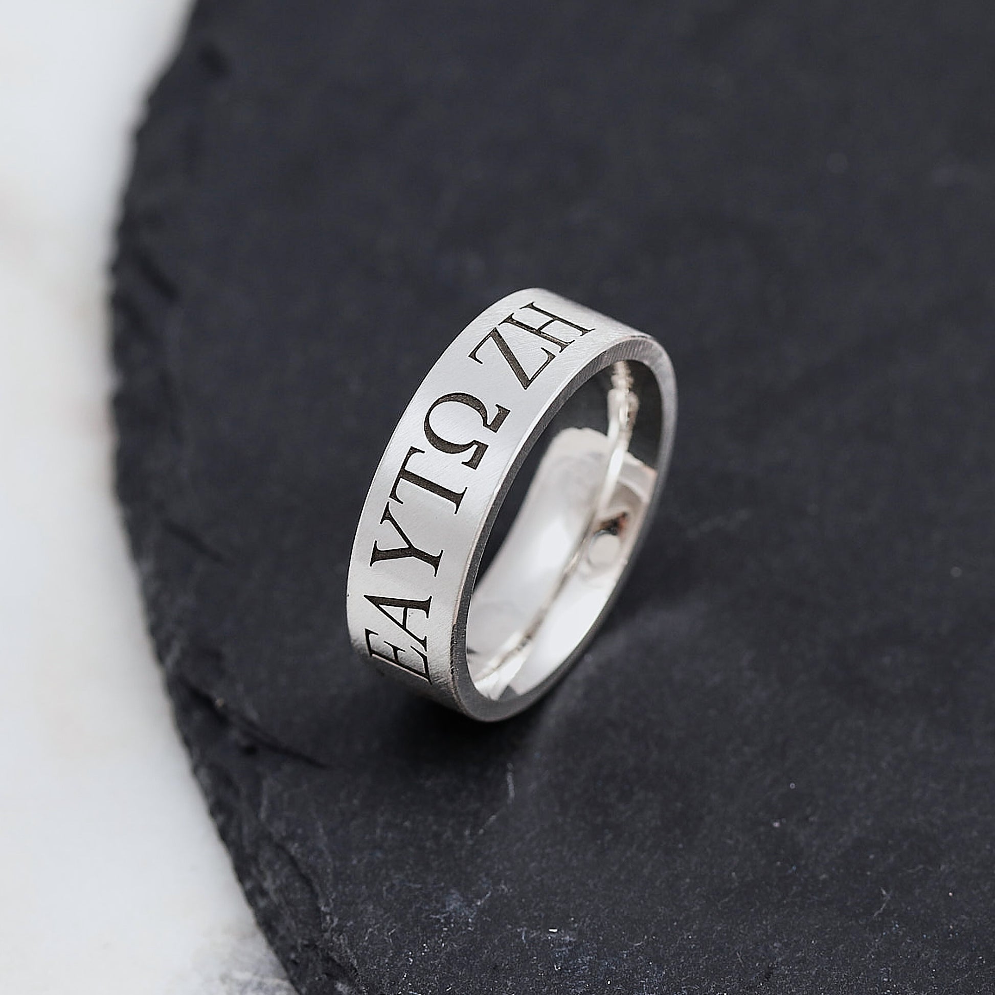 Silver ring with engraved text on a dark stone surface