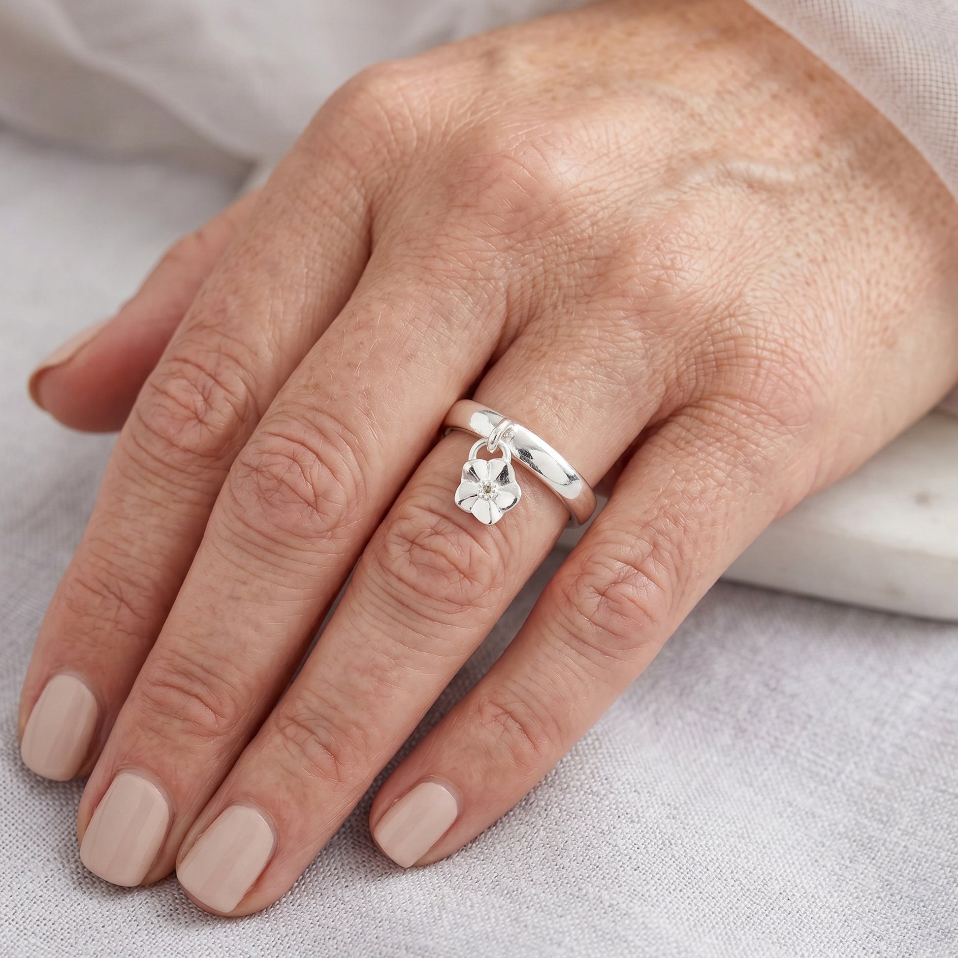 Silver ring with a  flower-shaped pendant on a hand against a neutral background
