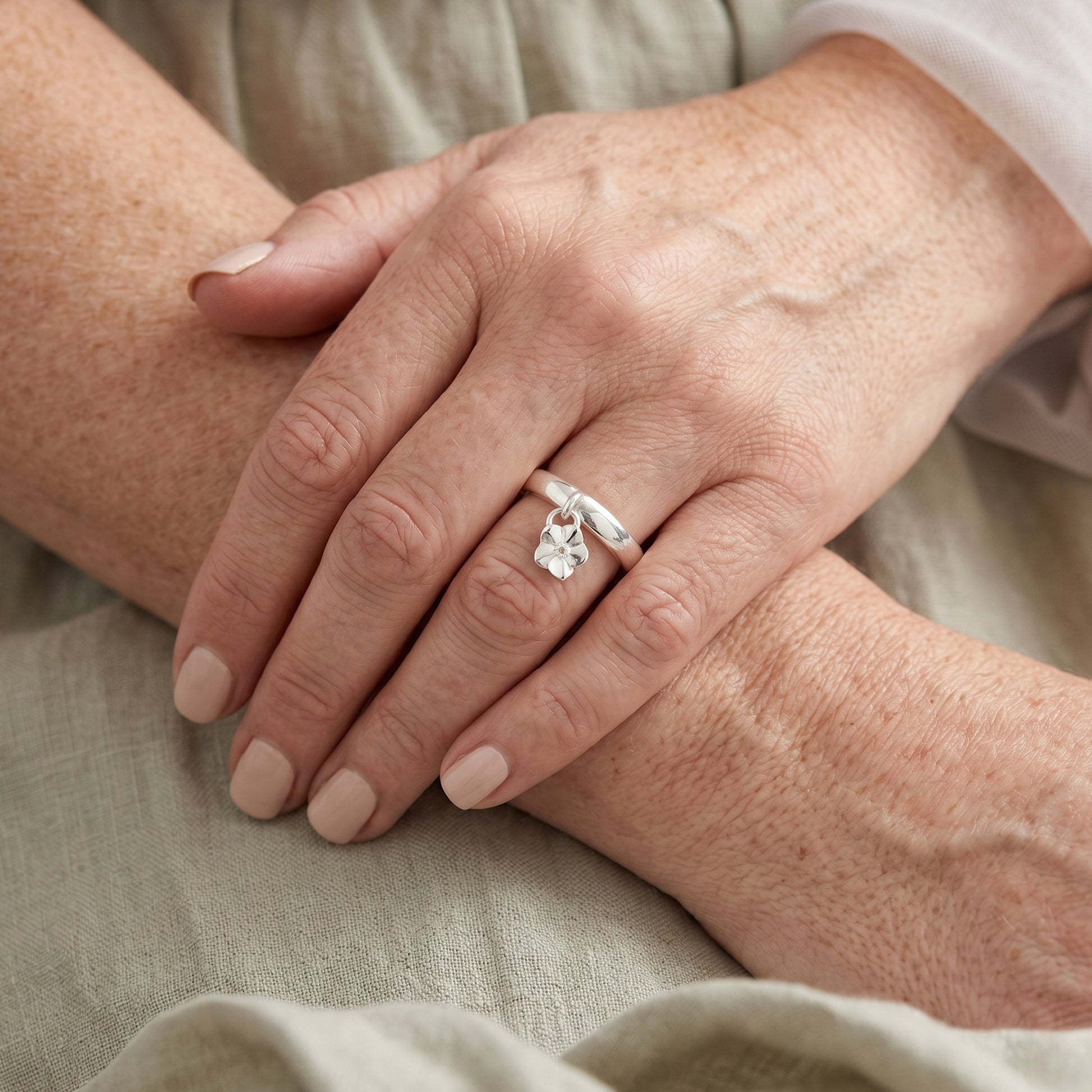 Close-up of hands with a silver ring featuring a flower on a beige fabric background