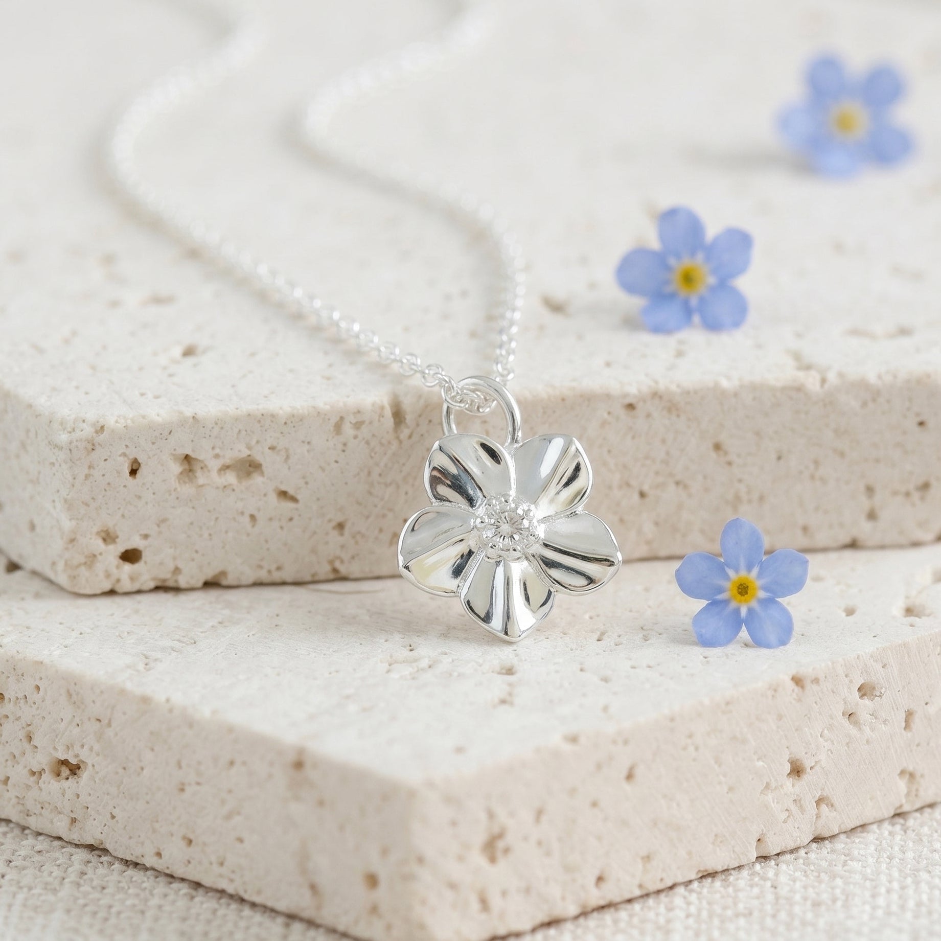 Silver flower necklace on a textured surface with small blue flowers.