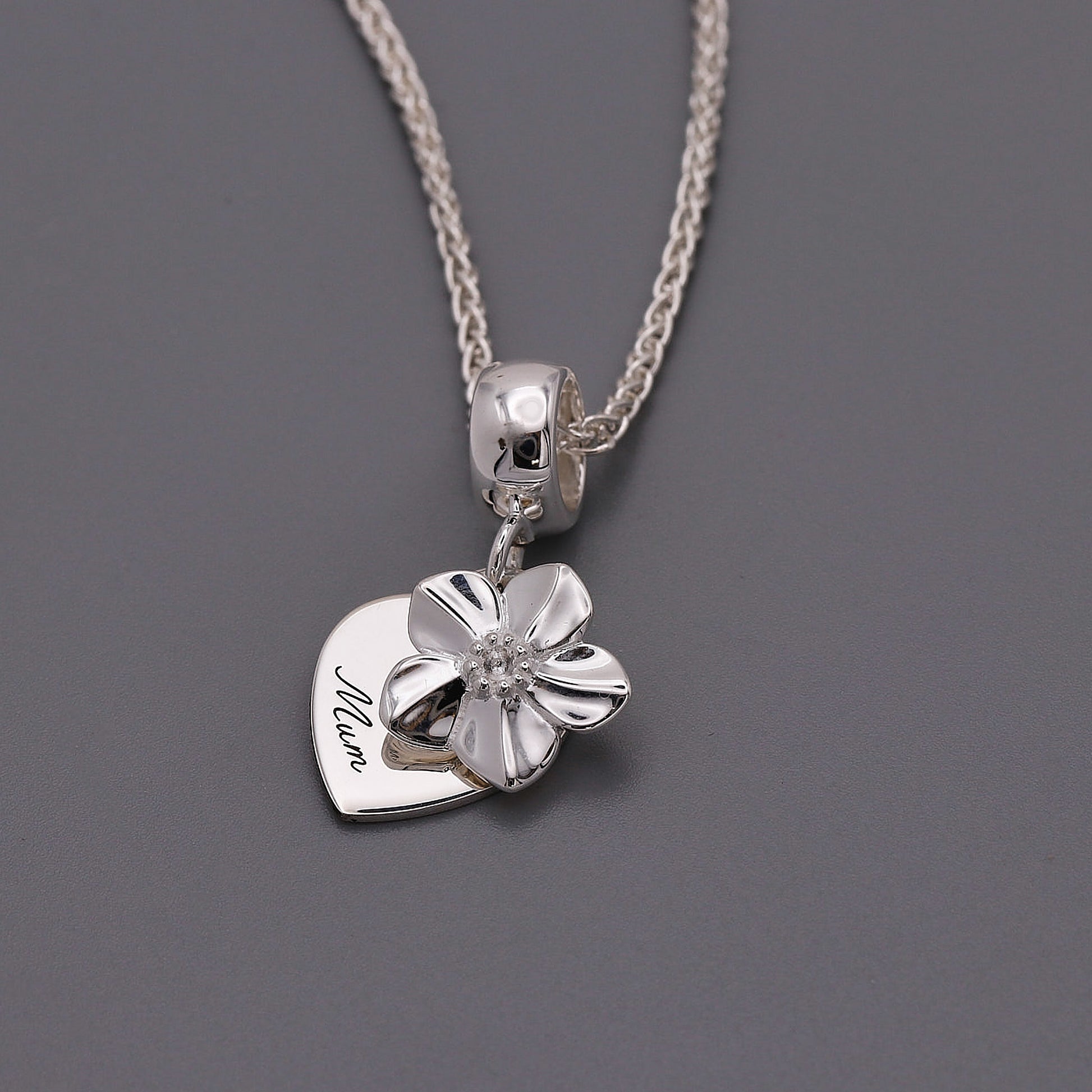 Silver necklace with a heart-shaped pendant and forget me not flower on a gray background