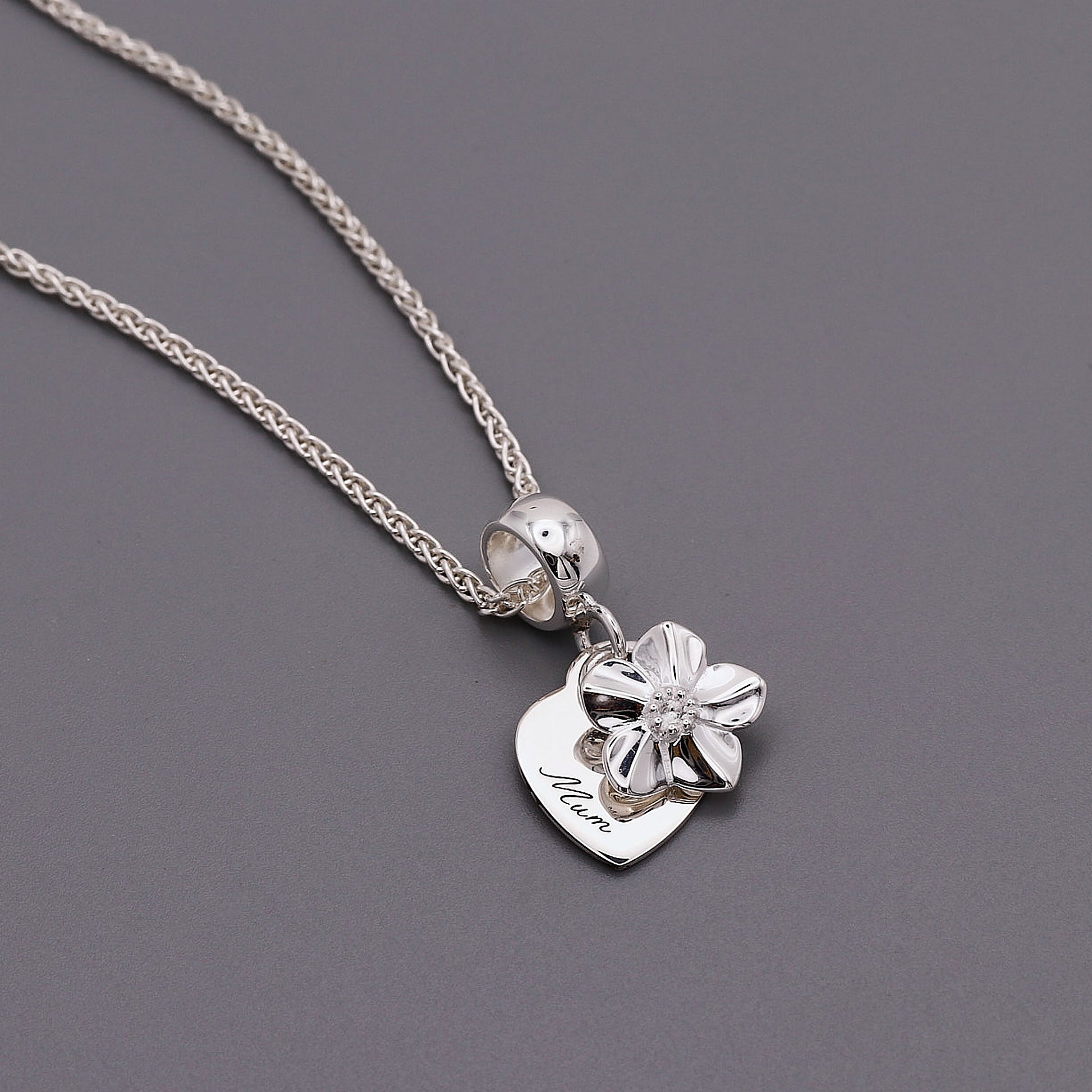 Silver necklace with a heart-shaped pendant and floral forget me not design on a gray background