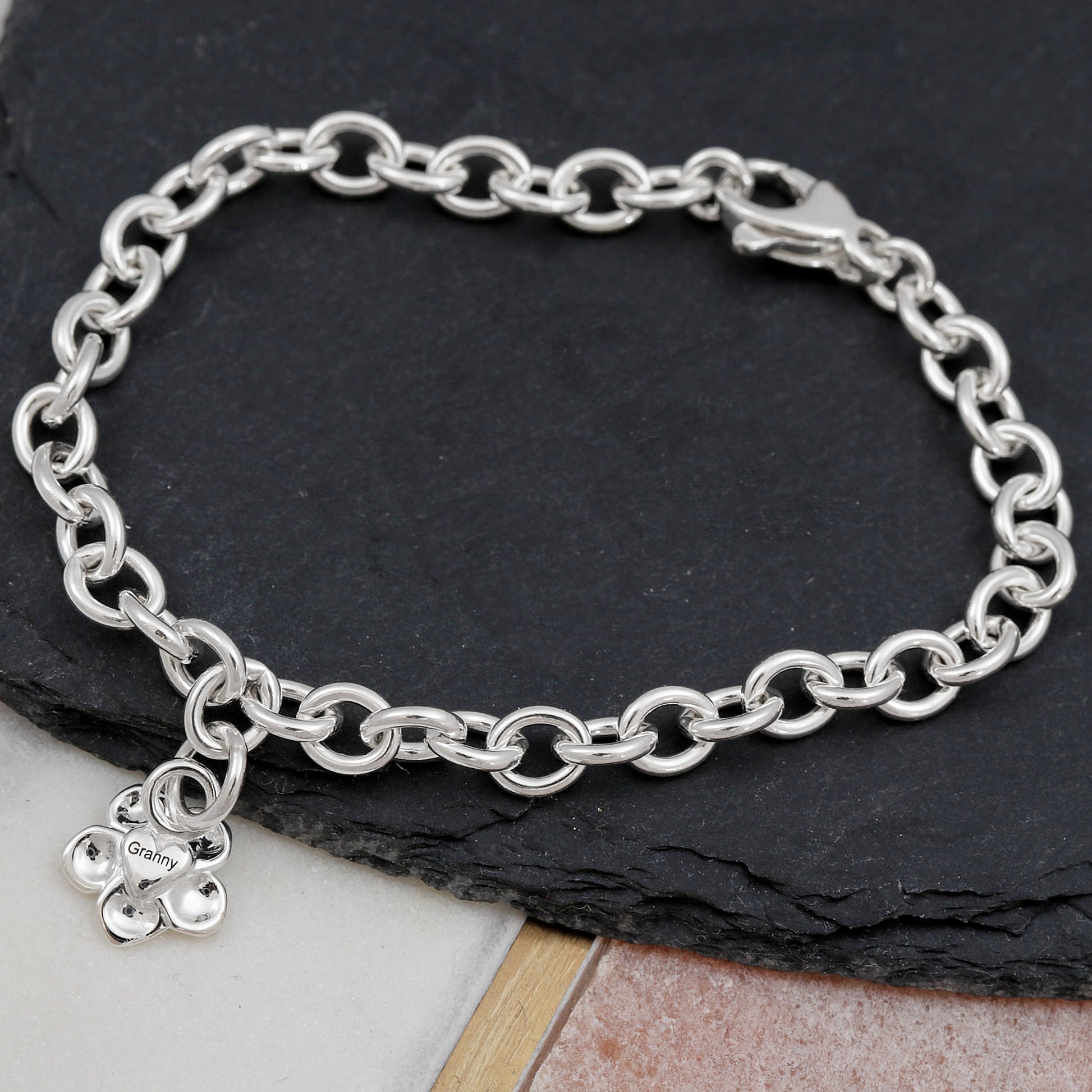 Silver chain bracelet with a flower charm on a dark stone surface