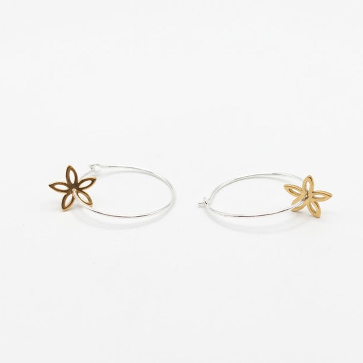 A pair of thin silver hoop earrings with small gold flower-shaped charms, displayed on a clean white background.