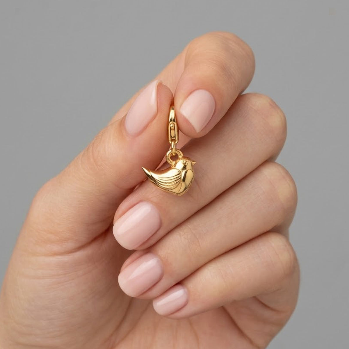 gold plated robin bird charm with clasp in a womans fingertips on grey background