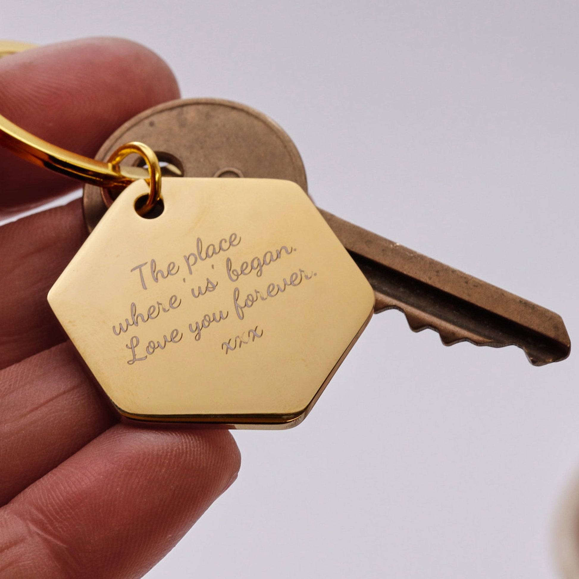 Gold keychain with engraved message held by a hand against a neutral background