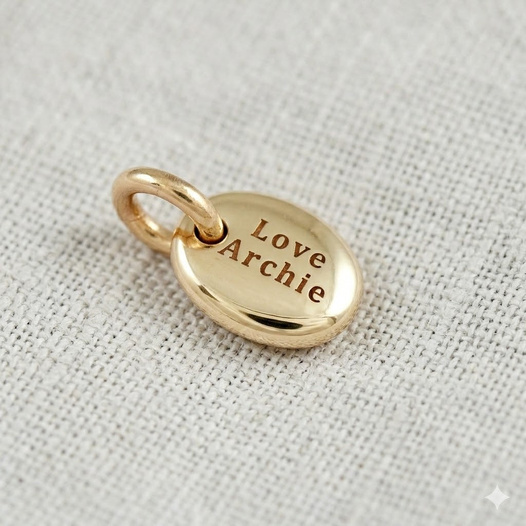 Gold pendant with 'Love Archie' engraving on a light fabric background